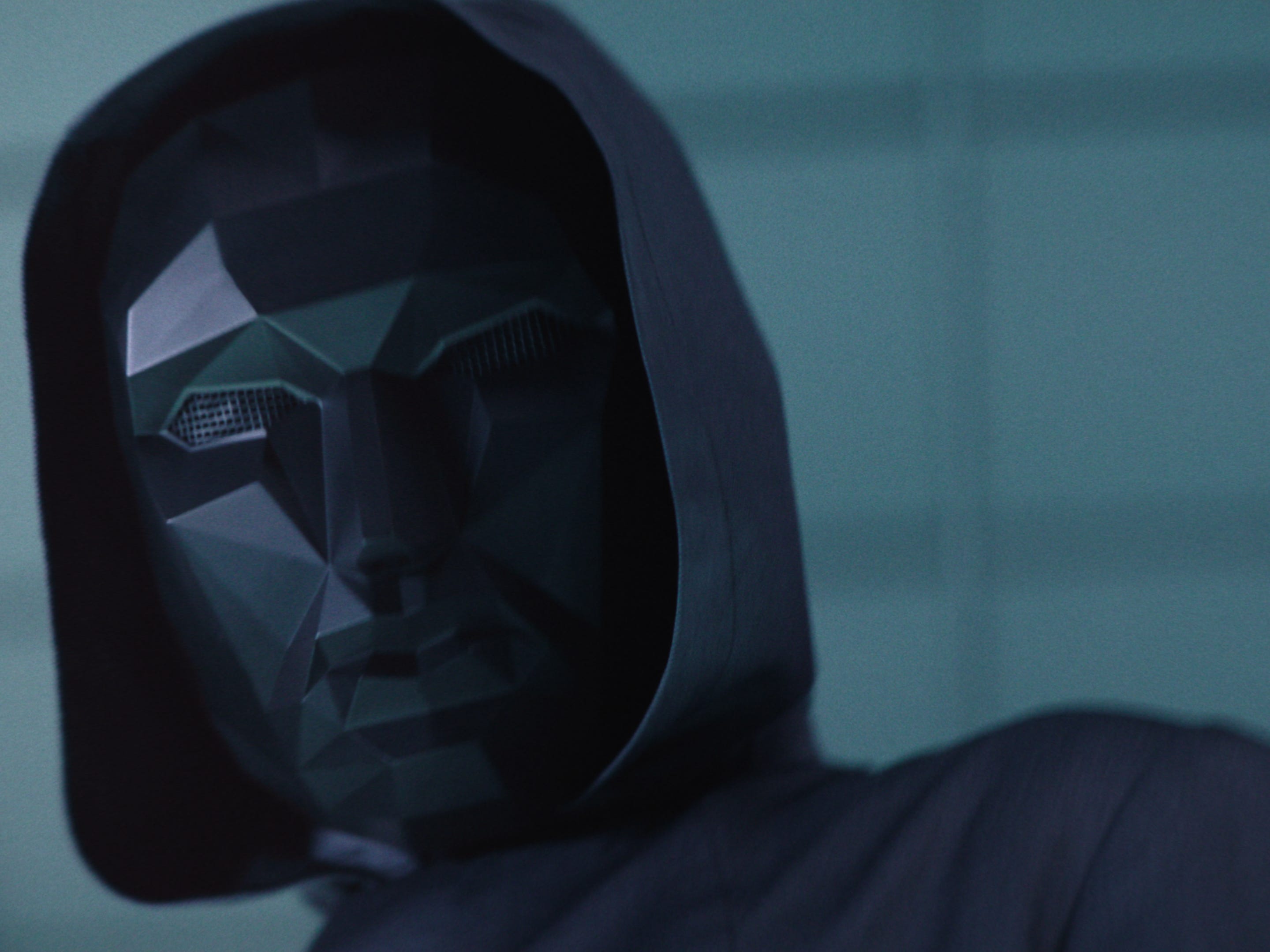 lee byung-hun as the front man in squid game. he's wearing an angular black face mask, and a black jacket with a hood that conceals his identity