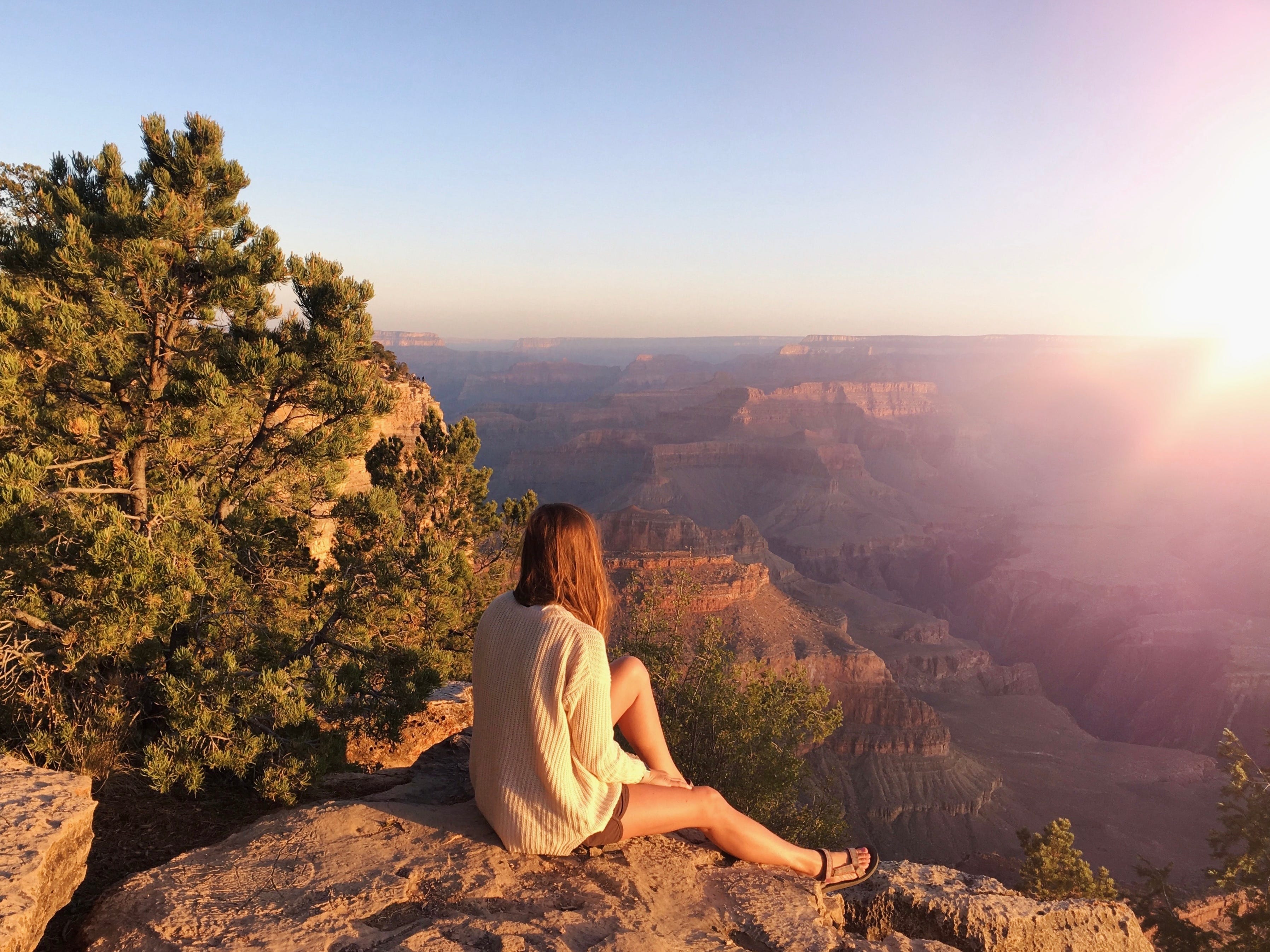 Emily sits on a rock and looks out at the sunrise over the Grand Canyon.