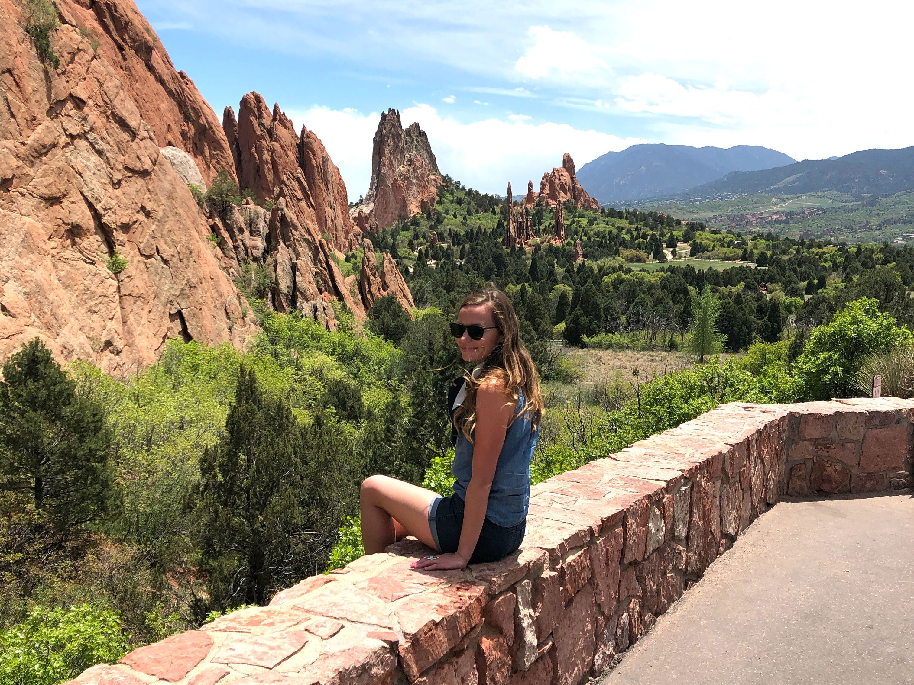 Emily sits on a wall near jagged red-rock formations.