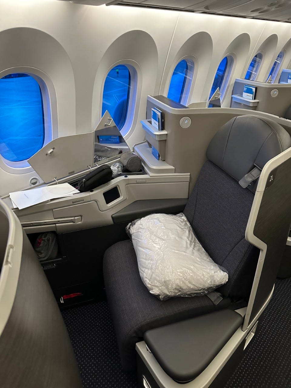 Business class seat on American Airlines flight with pillow, side storage compartment opened
