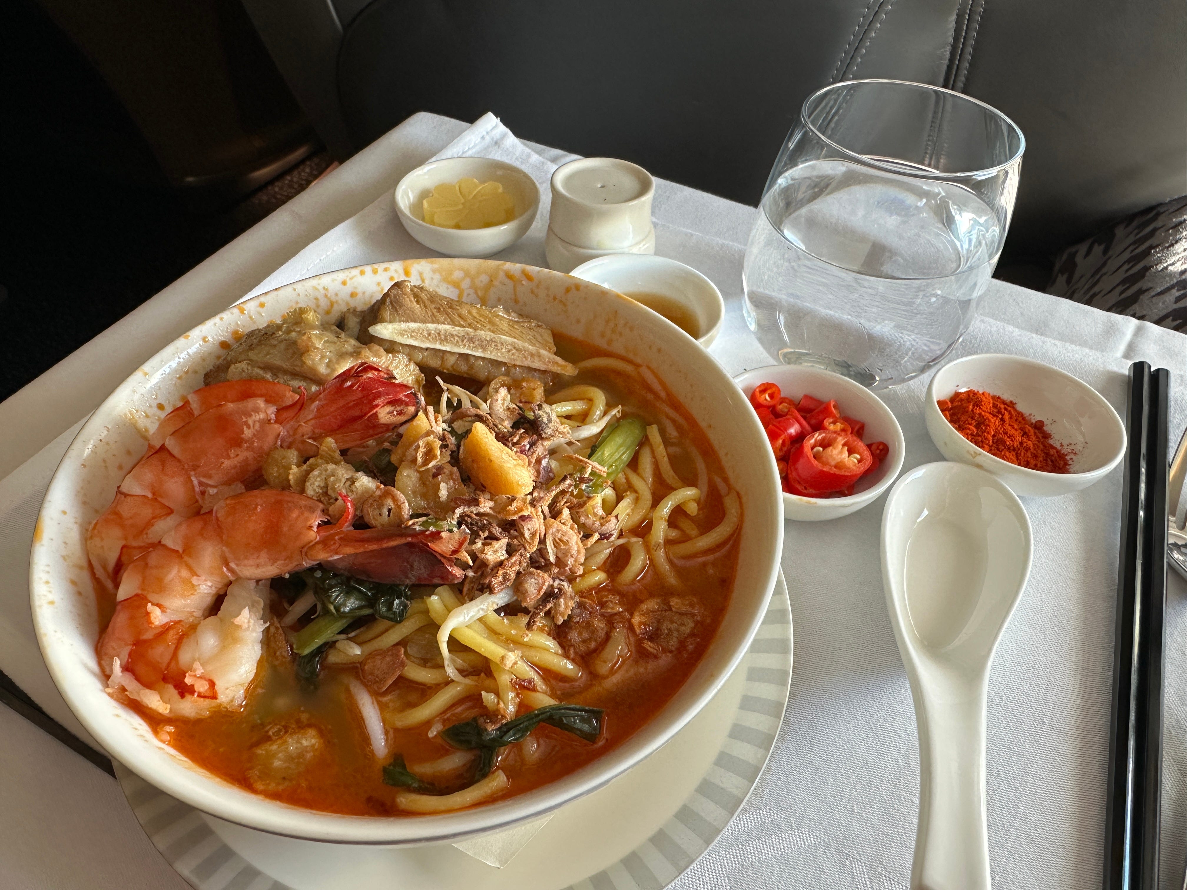 Ramen dish with shrimp on plane tray table with water, spoon, on Singapore Airlines flight