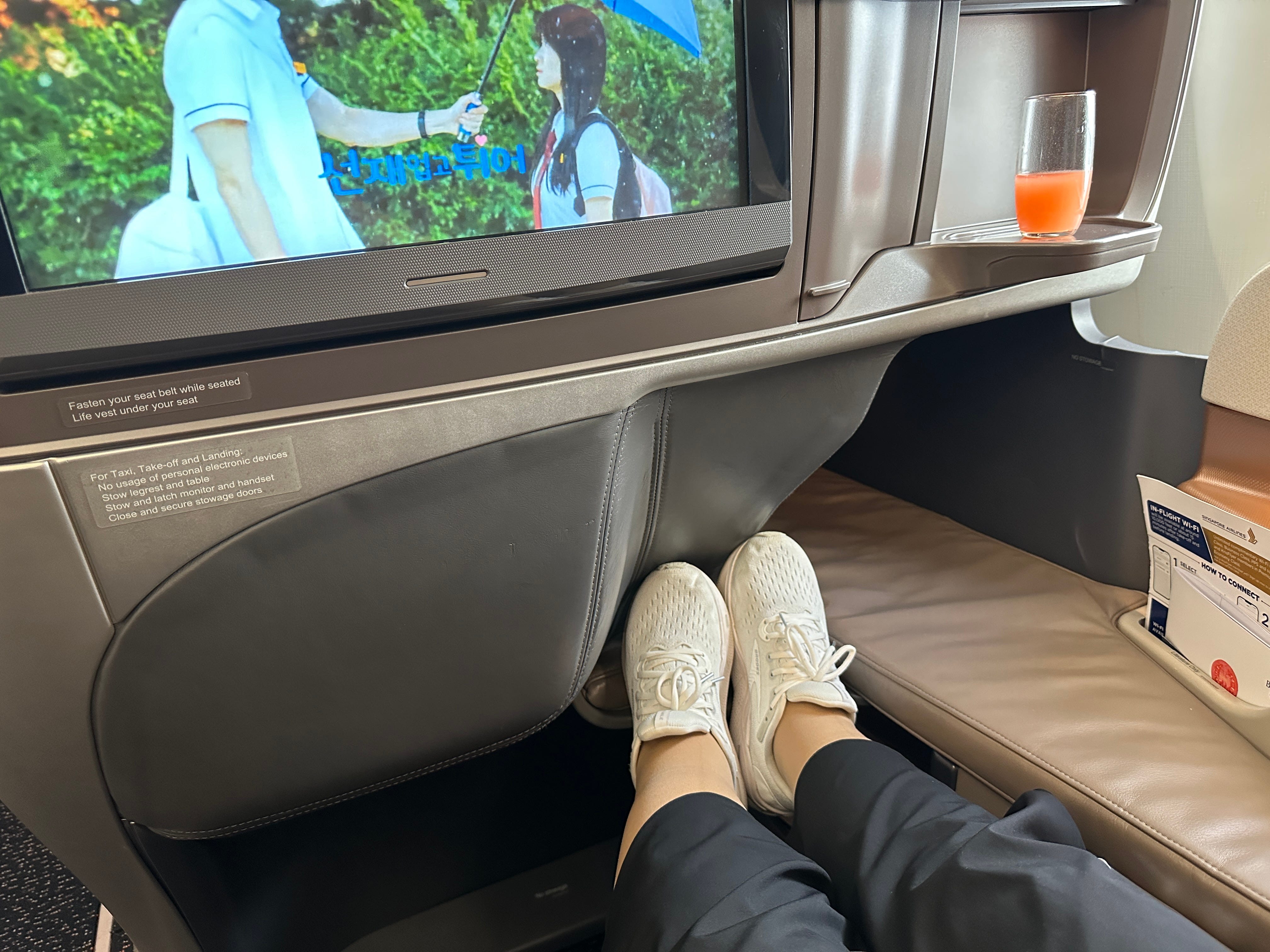 Feet touching end of business class seat with TV screen above