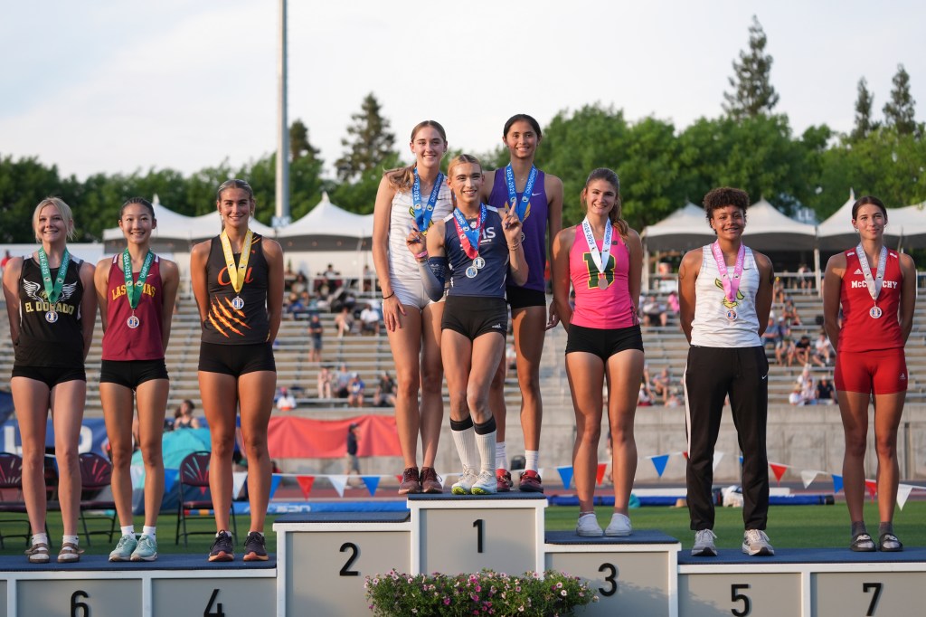 Seven female high school track athletes on a winners' podium, including AB Hernandez