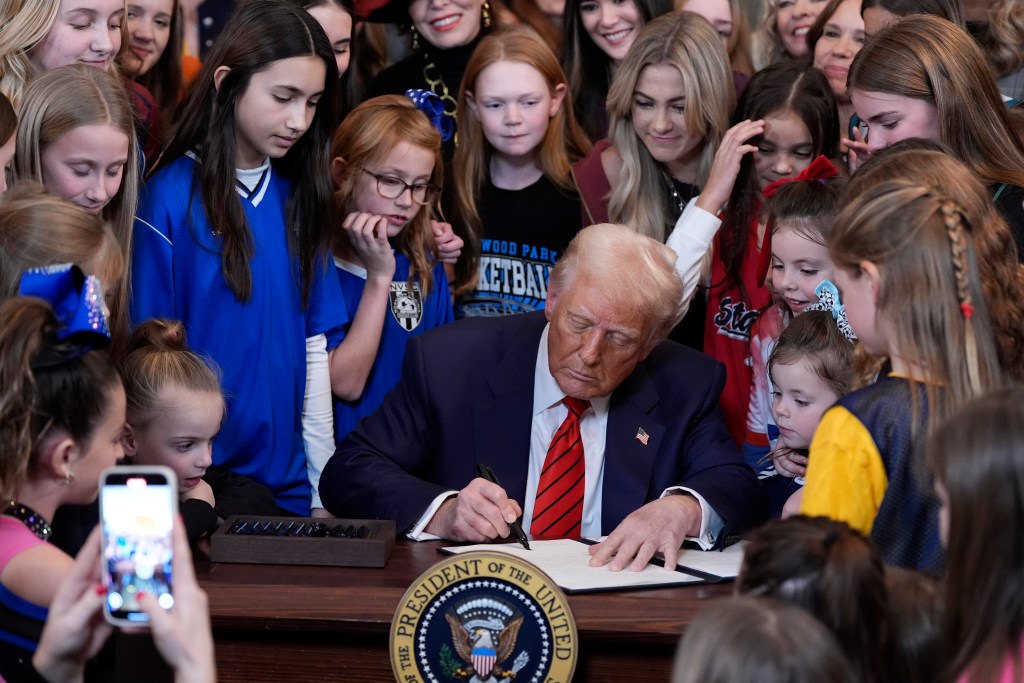 President Donald Trump signing executive order surrounded by female athletes.