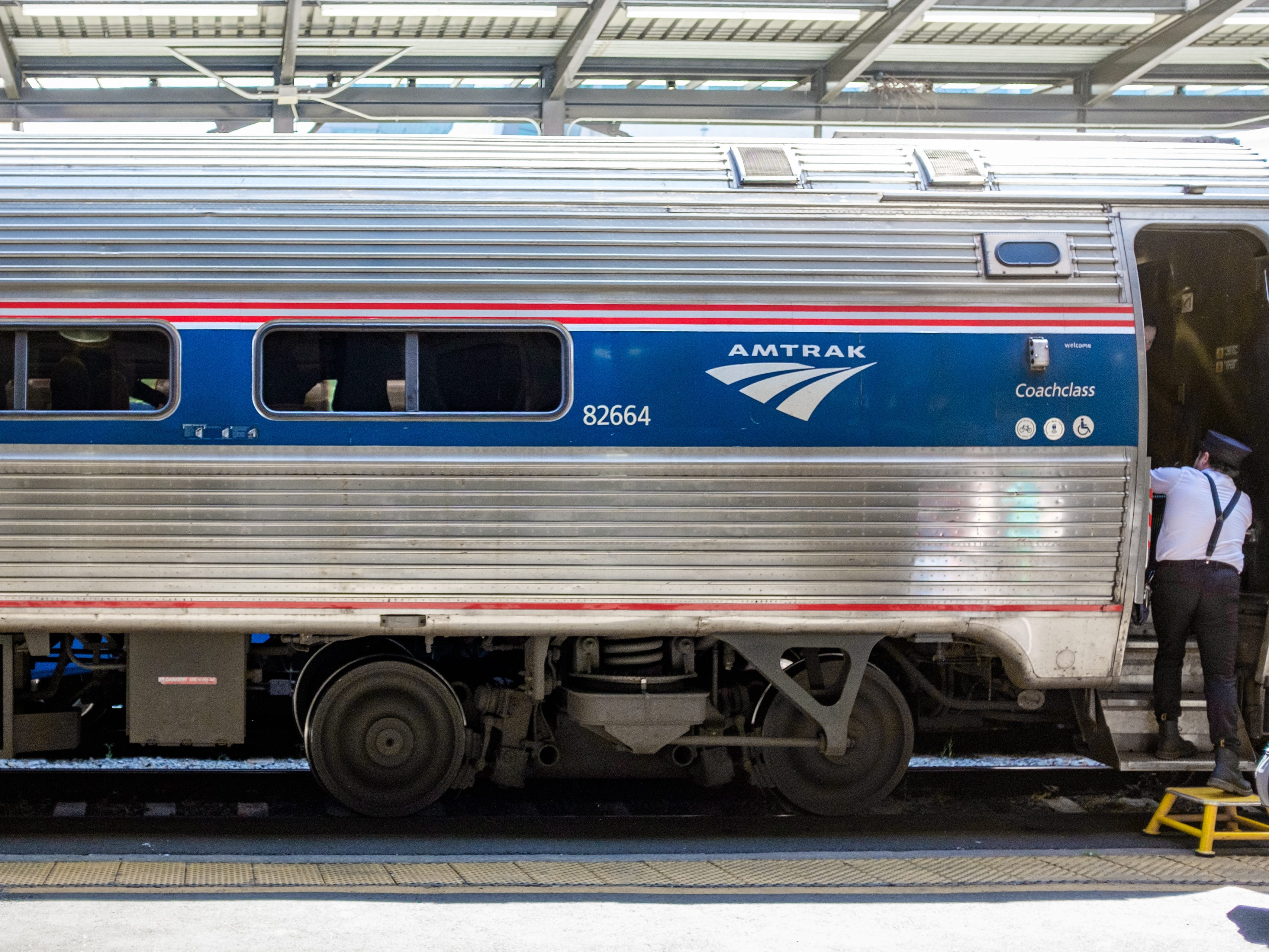 The exterior of a coach Amtrak train car with an attendant stepping out a door on the right