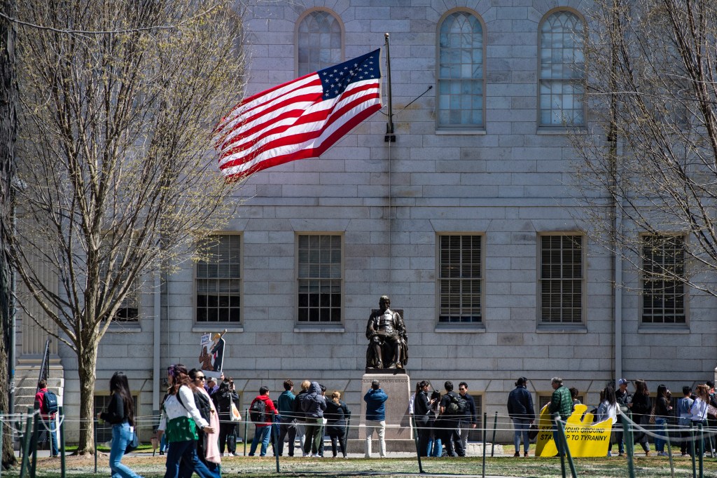 Demonstrators with signs stand around the John Harvard Statue in Harvard Yard following a rally against President Donald Trump's attacks on Harvard University at Harvard University in Cambridge, Massachusetts on April 17, 2025.