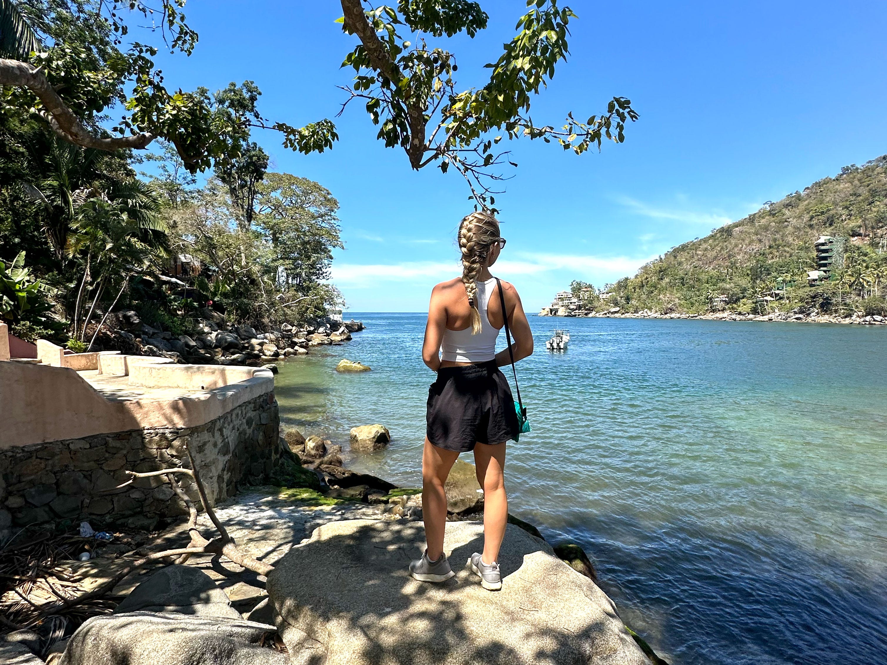 Chloe stands on a rock and looks out at a large body of water and tree-covered mountains.