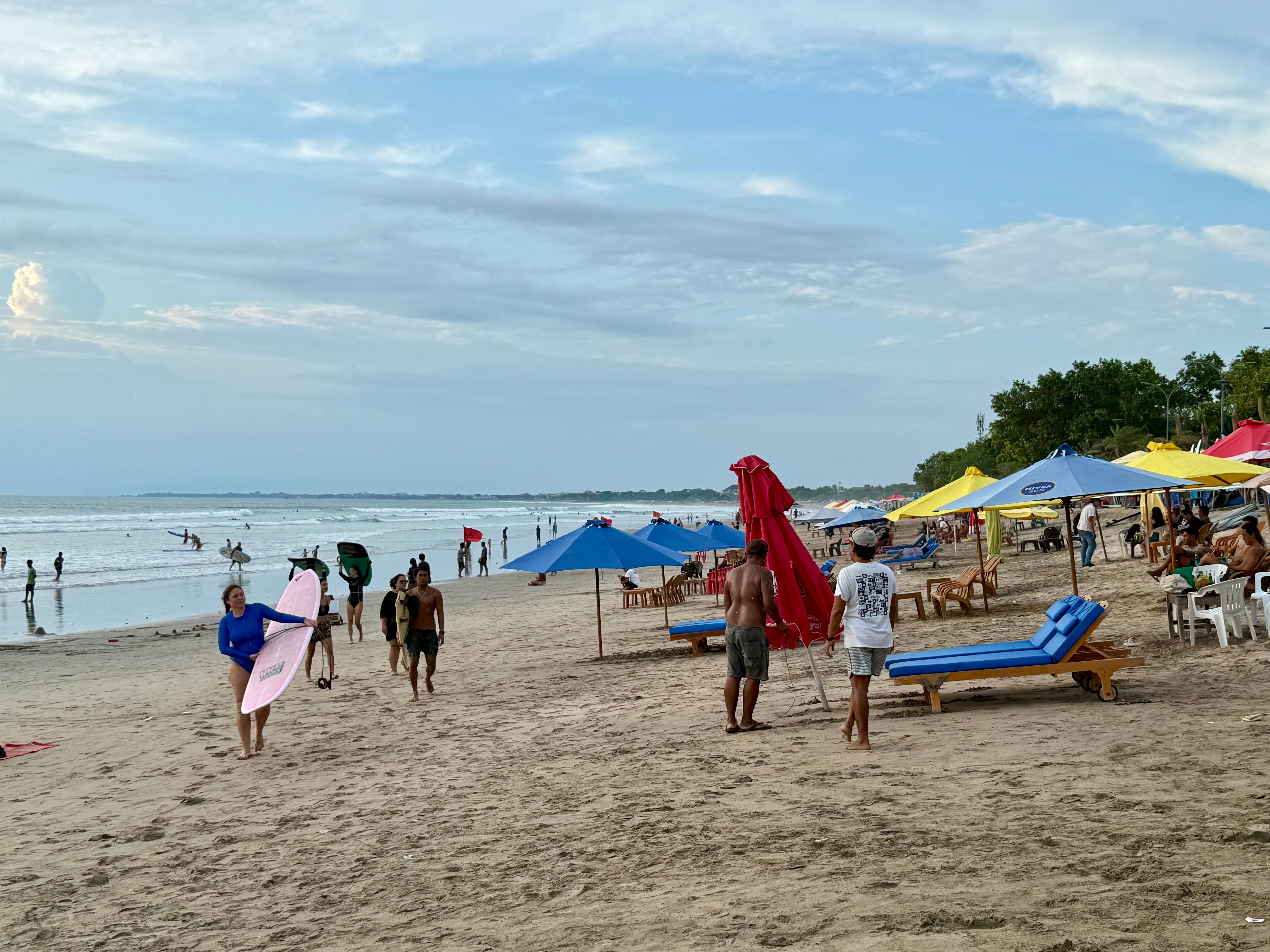 A shot of the beach in Bali with loungers, parasols and swimmers and surfers