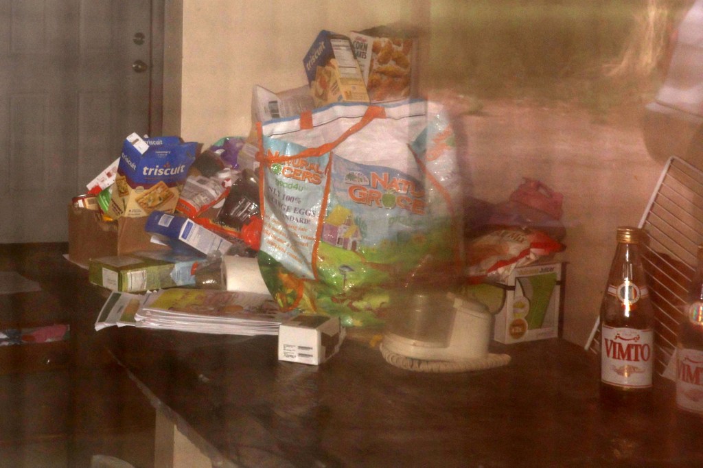 Messy countertop viewed through a window, showing various food items and a bottle of Vimto.
