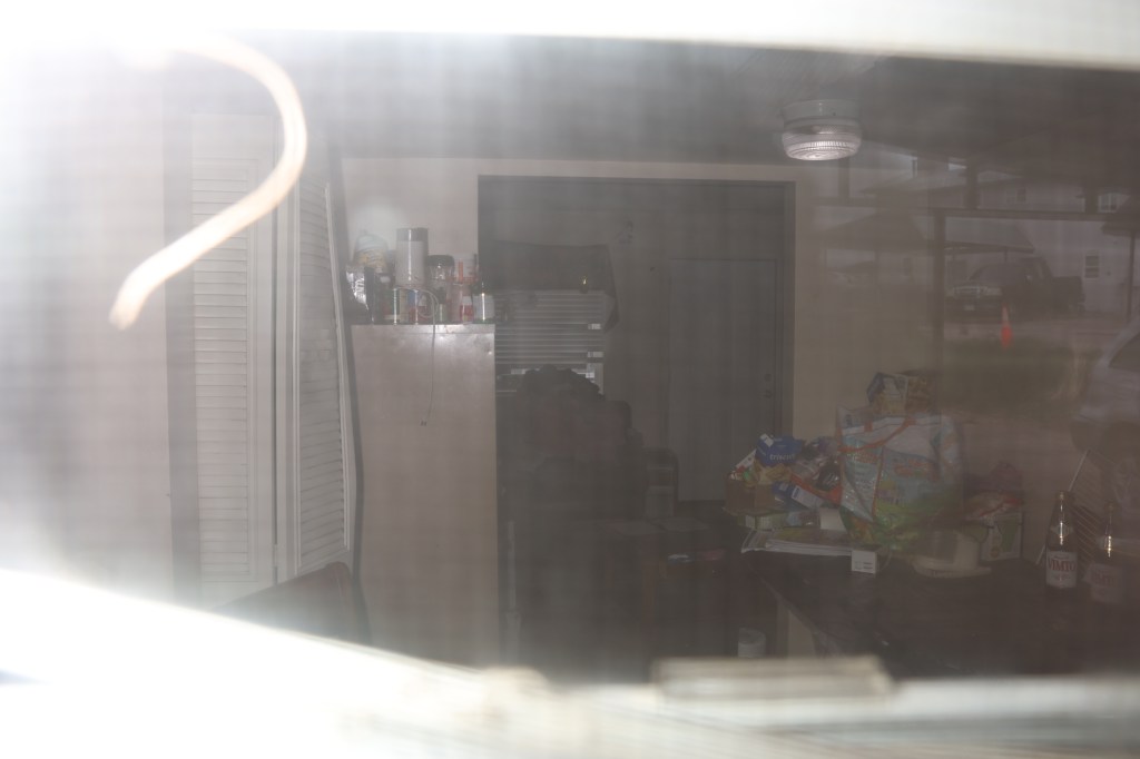 Messy interior of a home viewed through a dusty window.