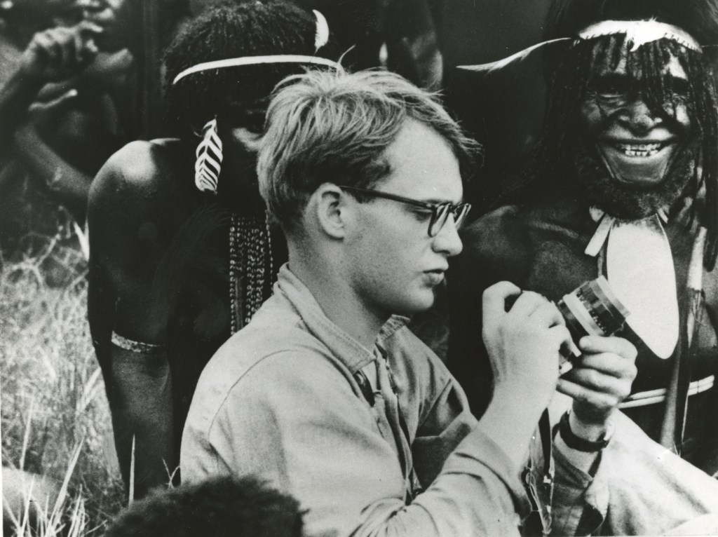 Black and white photo of Michael Rockefeller adjusting his camera in New Guinea.