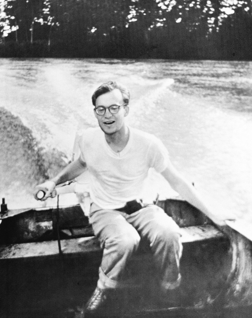 Black and white photo of Michael Rockefeller operating a motorboat in New Guinea.