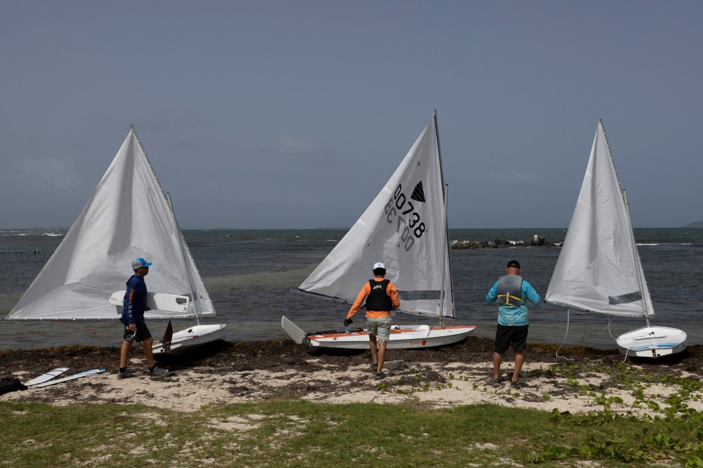 Three men prepare to launch their sailboats in Fajardo, Puerto rico on top of the sargassum seaweed.