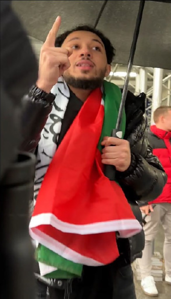 Tarek Bazrouk, under an umbrella, wearing a Palestinian flag and gesturing.