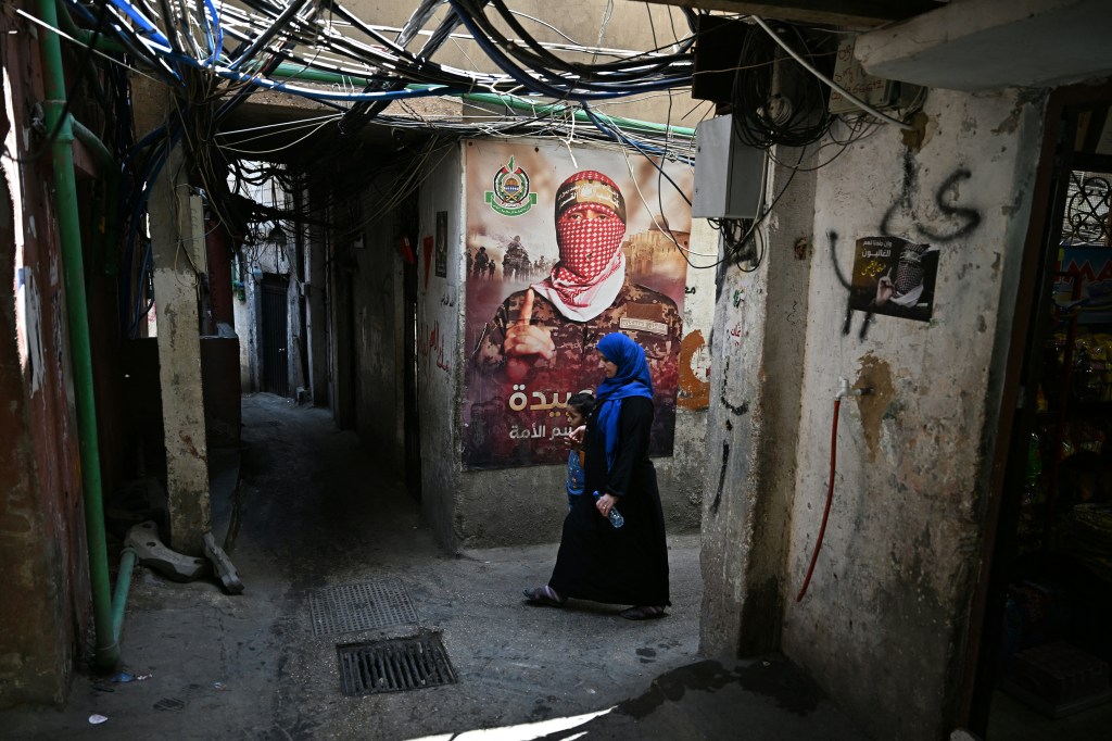 A woman walks past a poster of Abu Obaida in a Palestinian refugee camp.