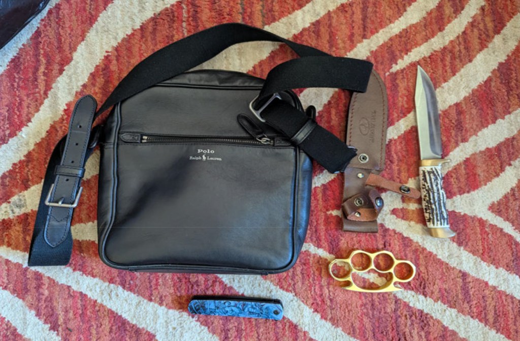 Bag, knife, brass knuckles, and pocketknife on a rug.