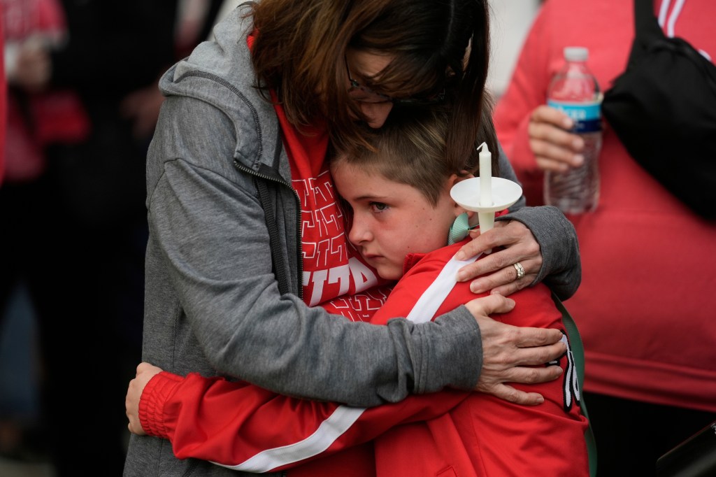 A woman hugs a child at a vigil following a car crash.