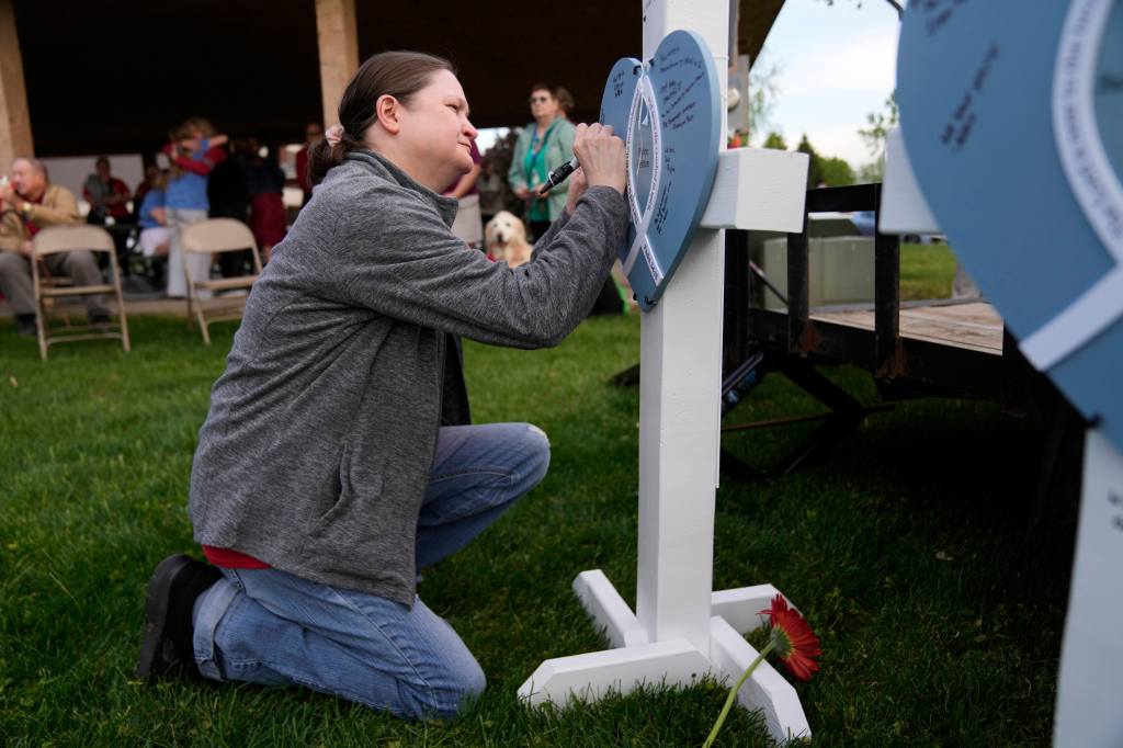 Woman writing on a heart-shaped memorial at a vigil.