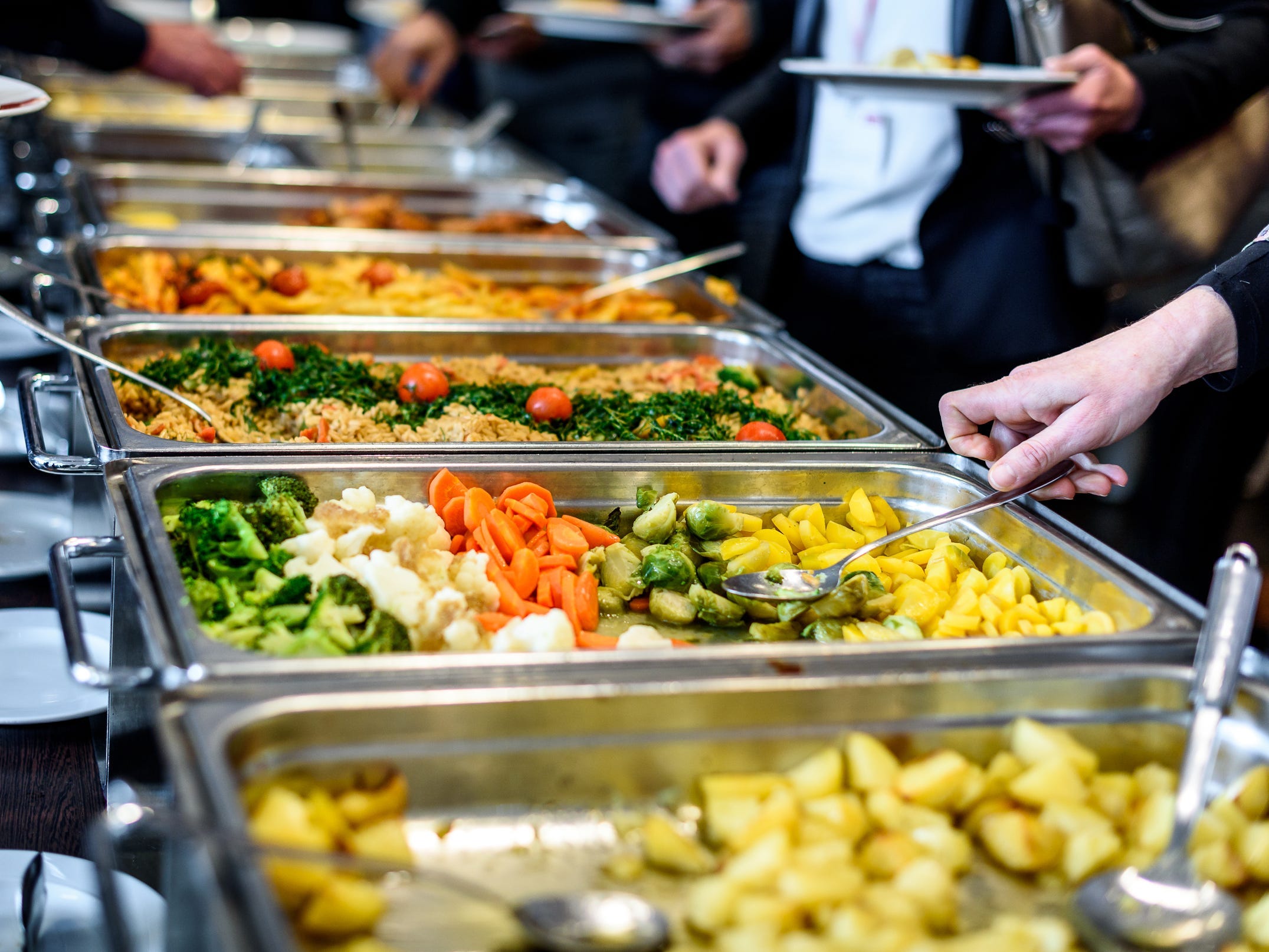 People taking food from trays at a buffet.