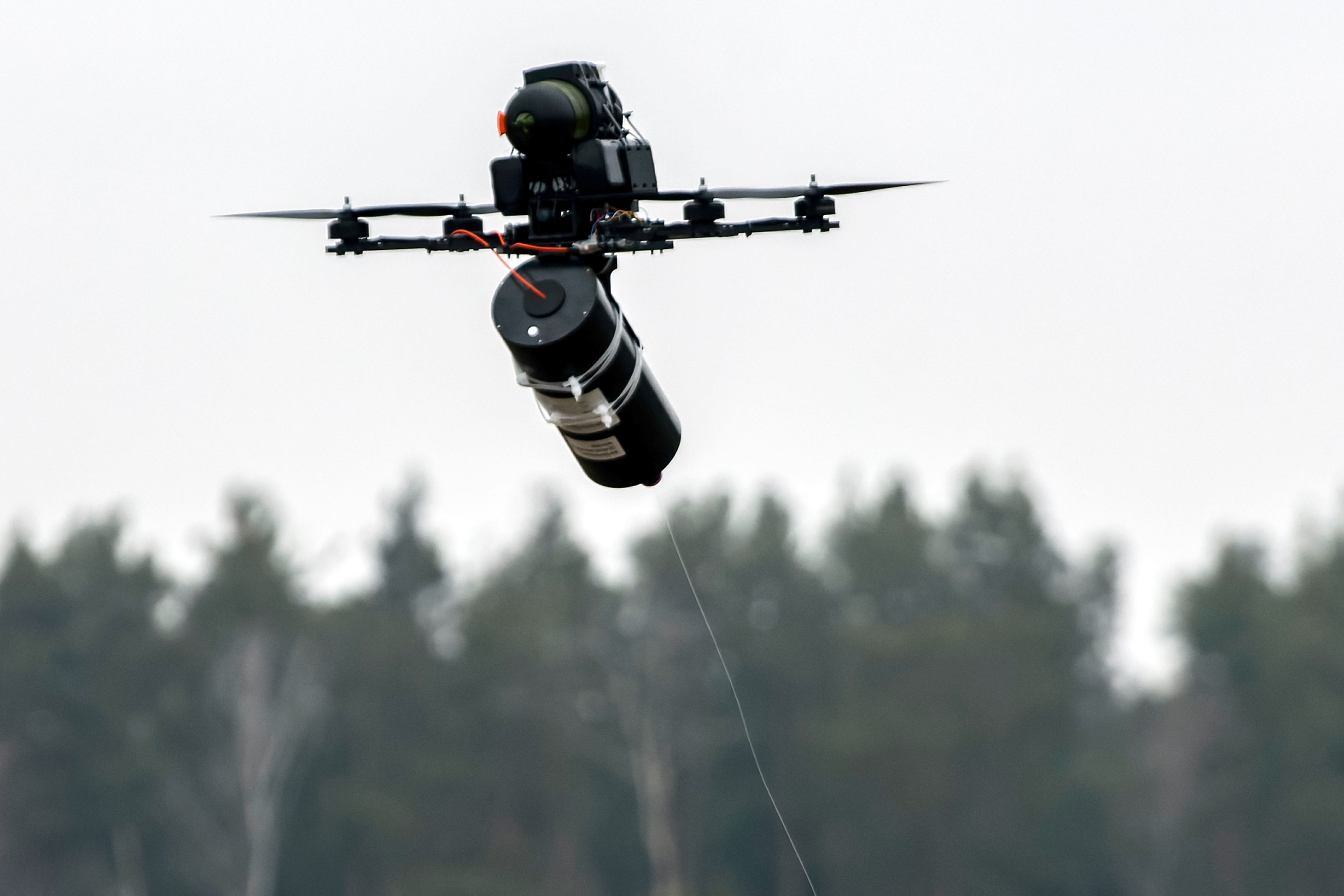 A fiber-optic drone flying with trees in the background.