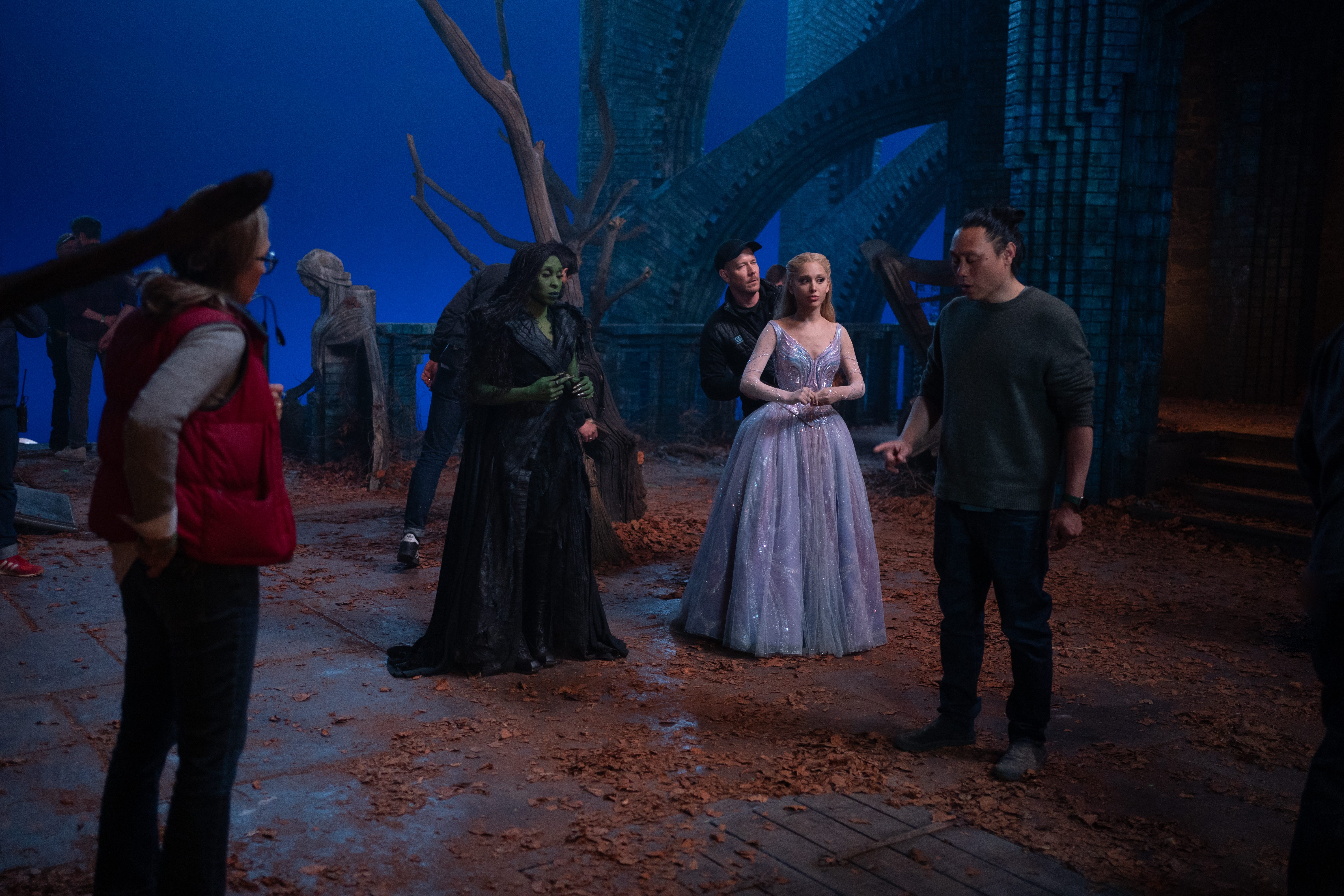 A still of the "Wicked: For Good" set showing Cynthia Erivo, Ariana Grande in costume and Jon M. Chu with crew around them.