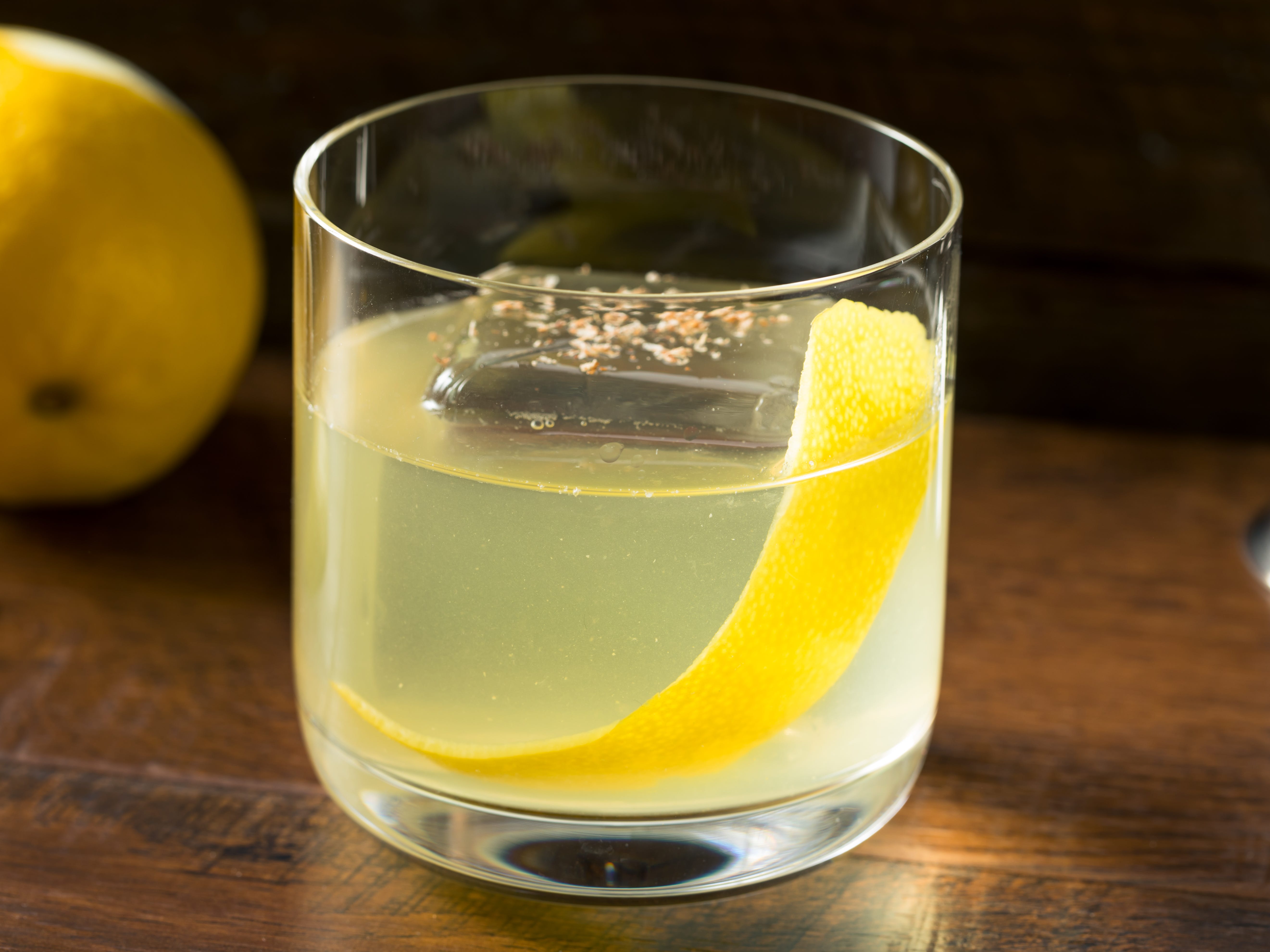 A clarified cocktail with a lemon peel and a large ice cube.