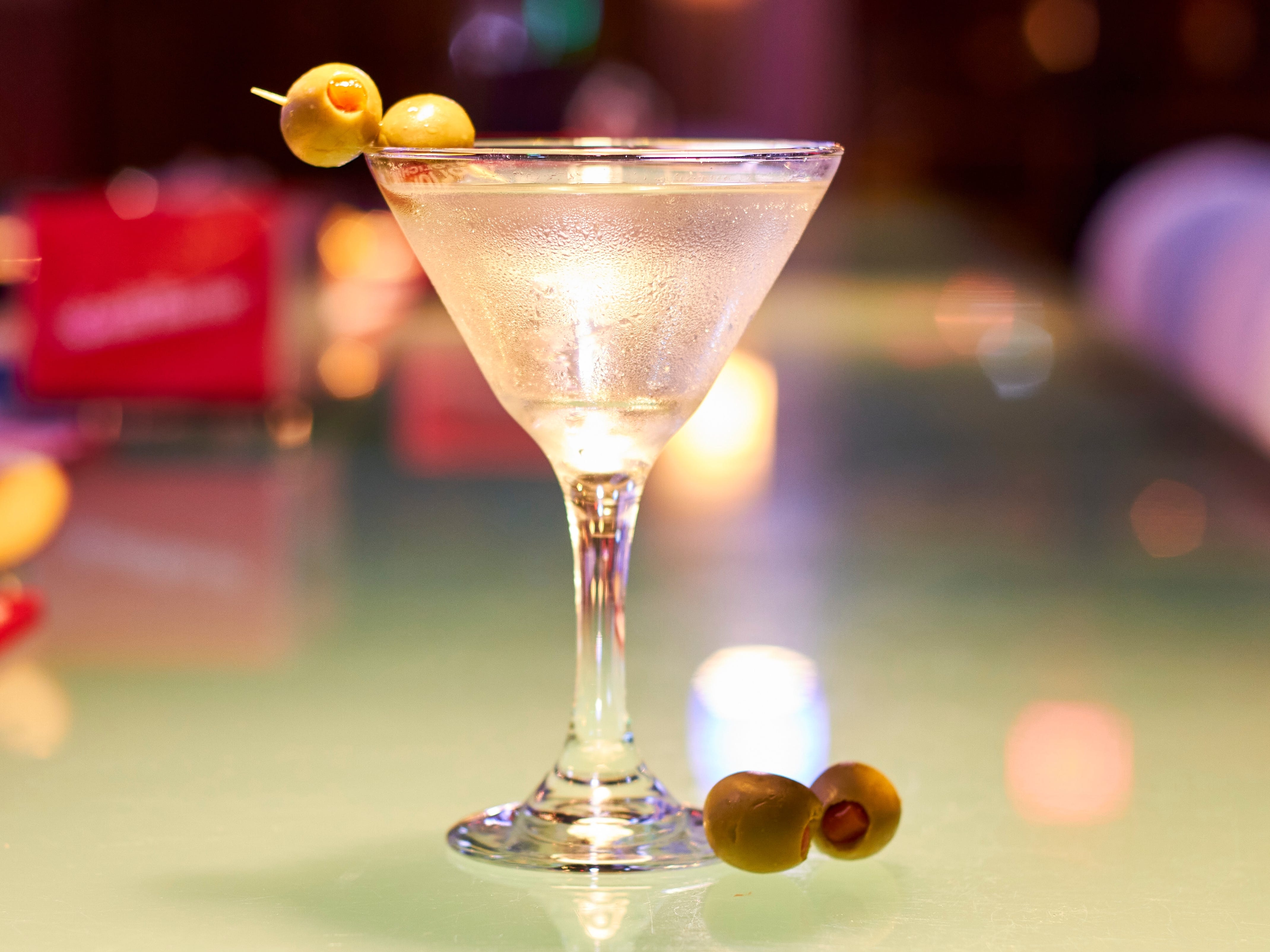A dirty martini with two olives on a bar.