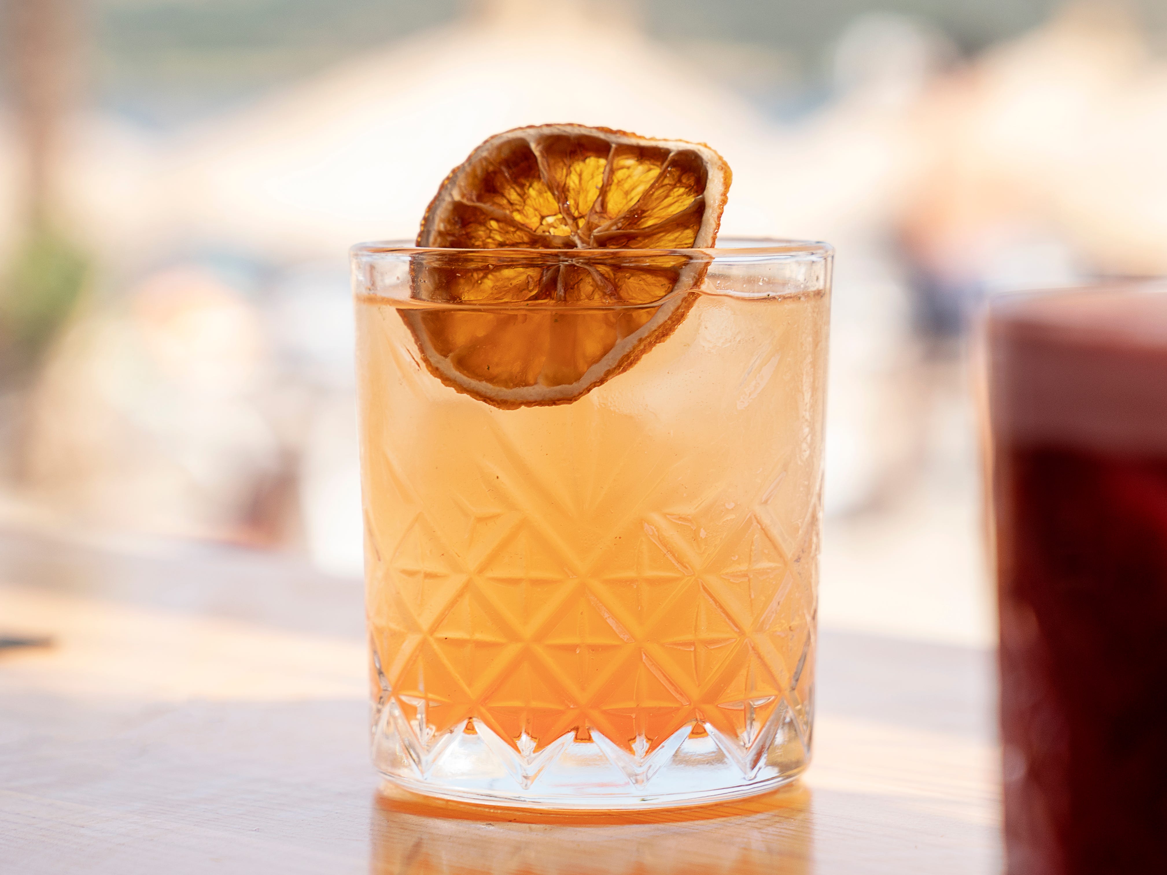 An orange juice cocktail garnished with a dried orange slice on a beach bar.