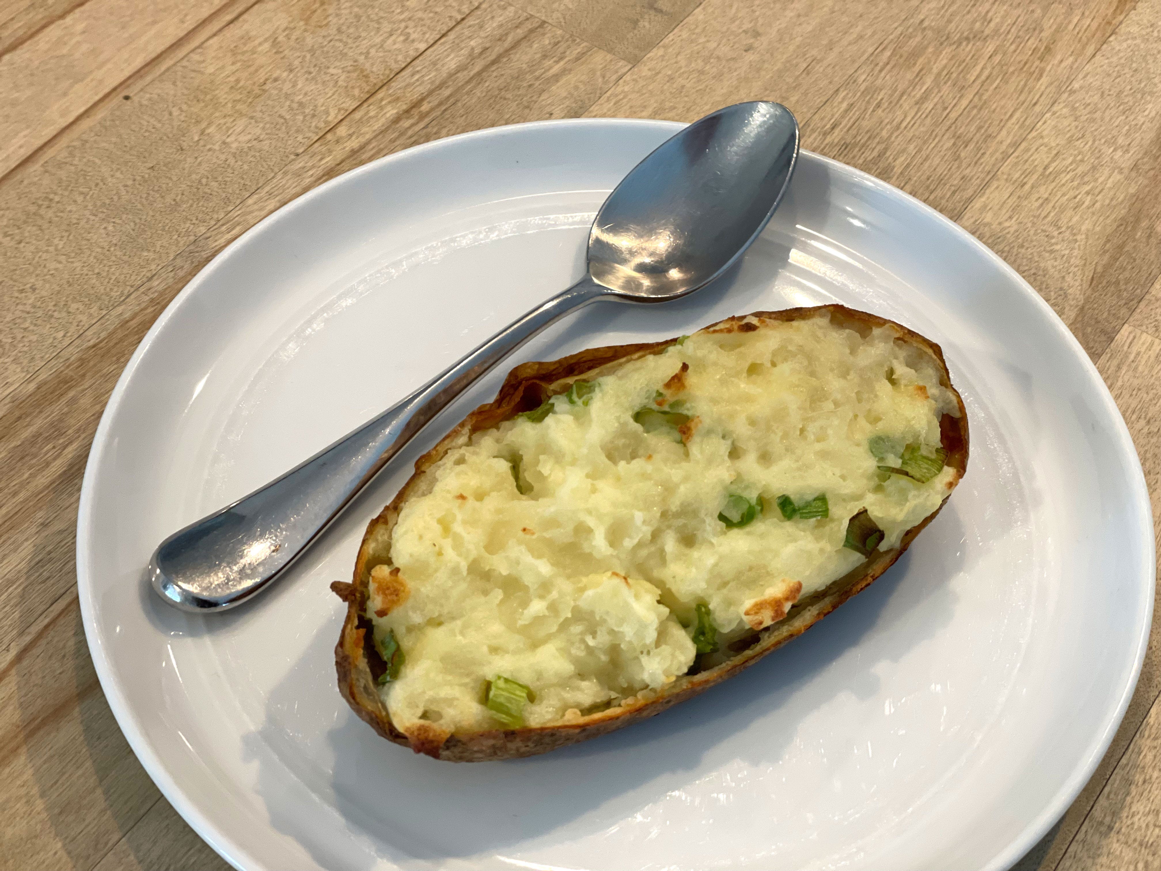 A twice-baked potato and a spoon on a white plate.