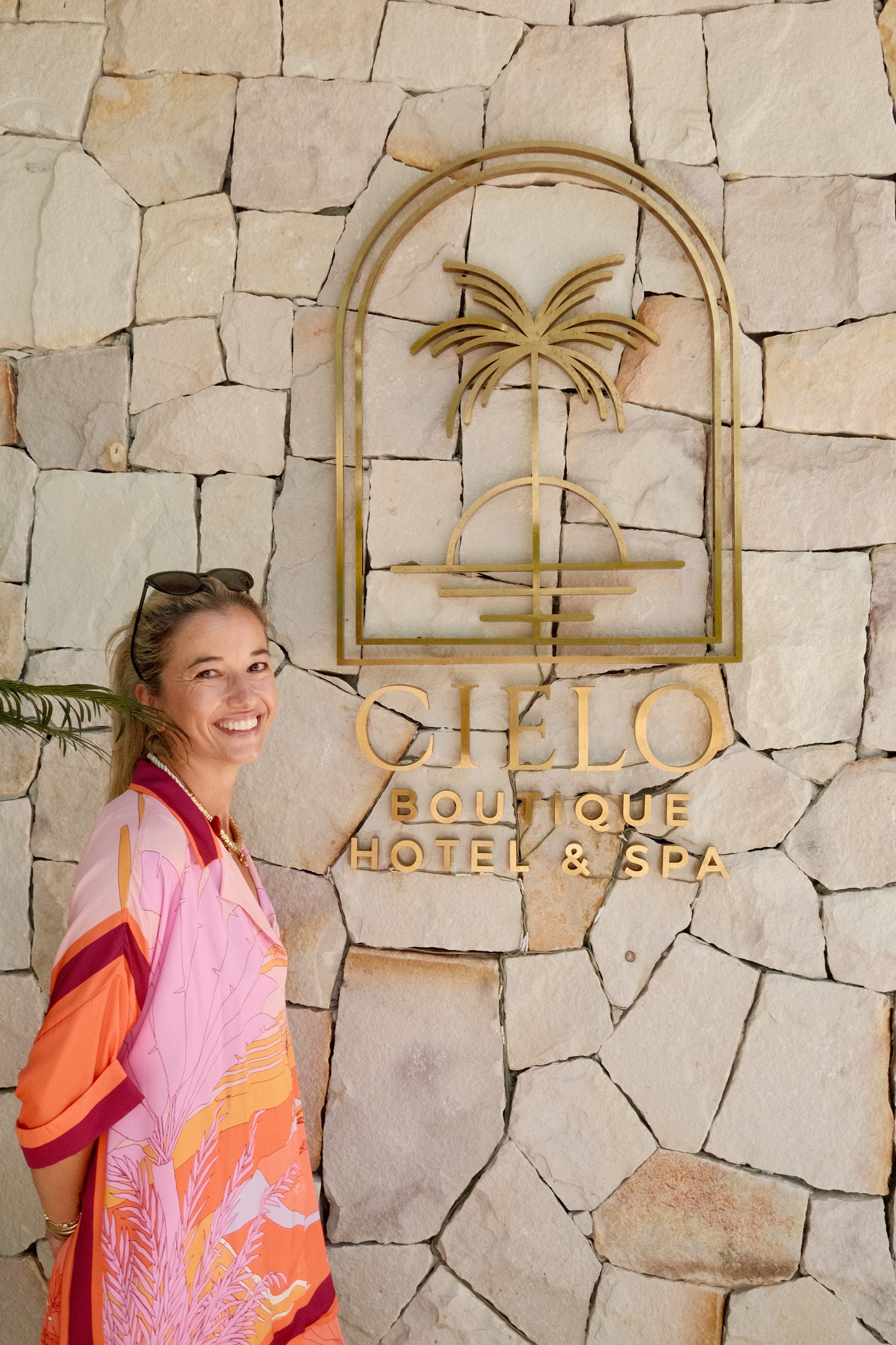 A woman in a colorful outfit posing in front of a metal boutique hotel sign.