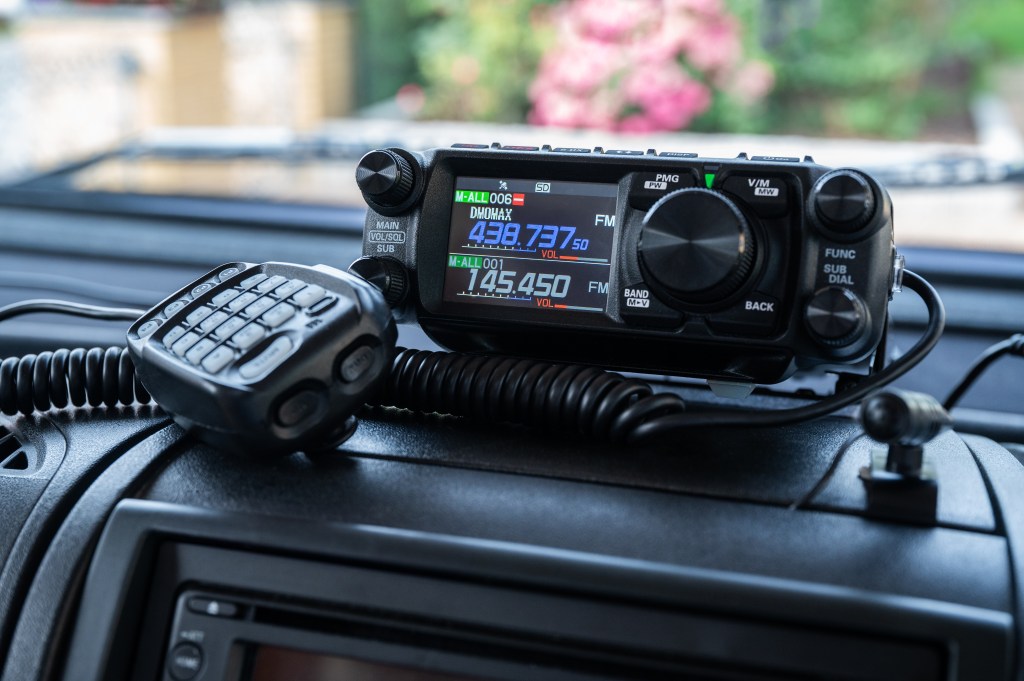 Mobile amateur radio transceiver with microphone on a car dashboard.