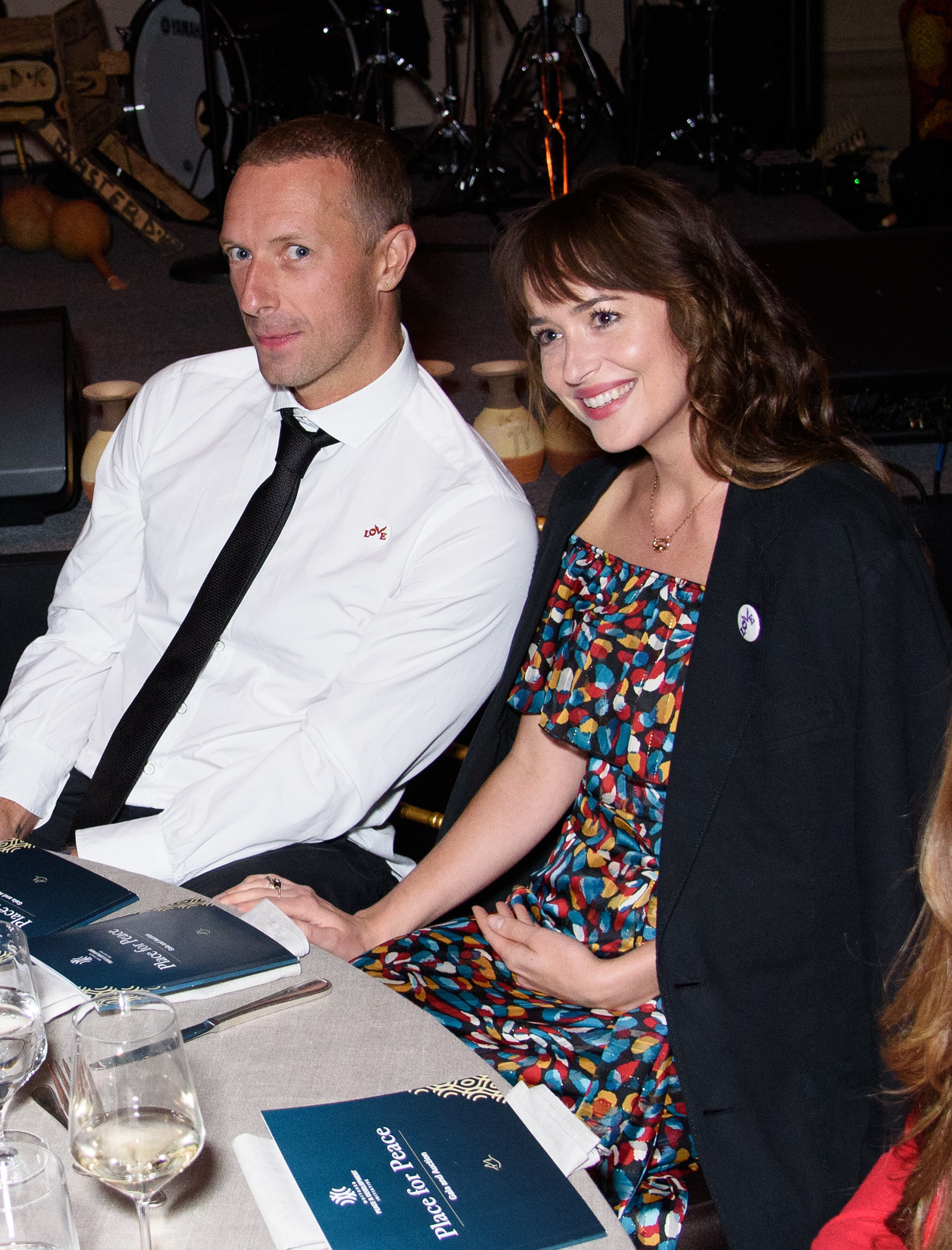 Dakota Johnson and Chris Martin smile at a table. 