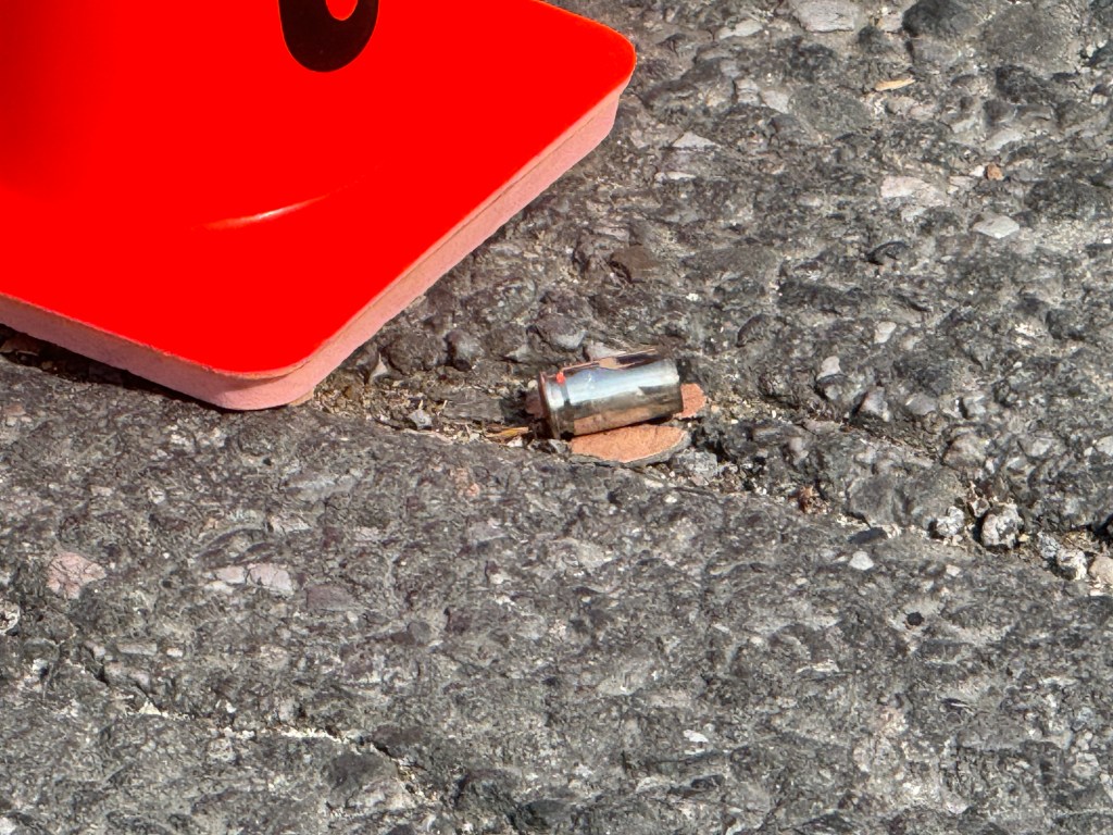 Spent shell casing on the ground near a red traffic cone.