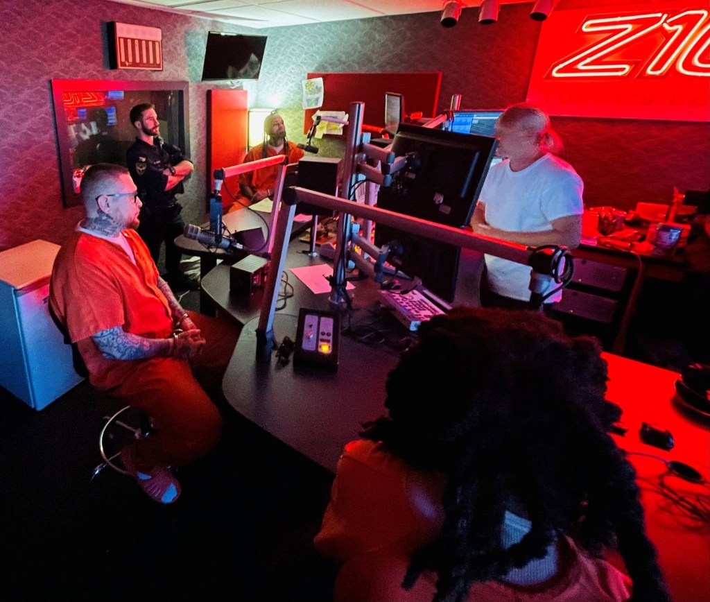 A man in an orange jumpsuit is being interviewed in a radio station.