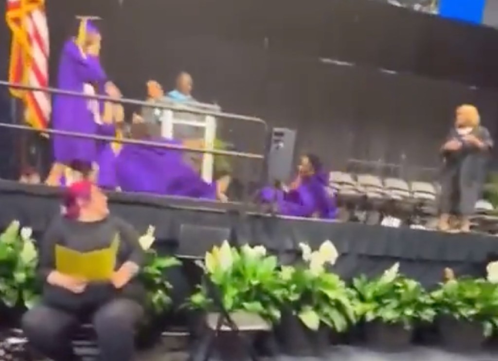A student accidentally knocks over another student during a backflip at a graduation ceremony.