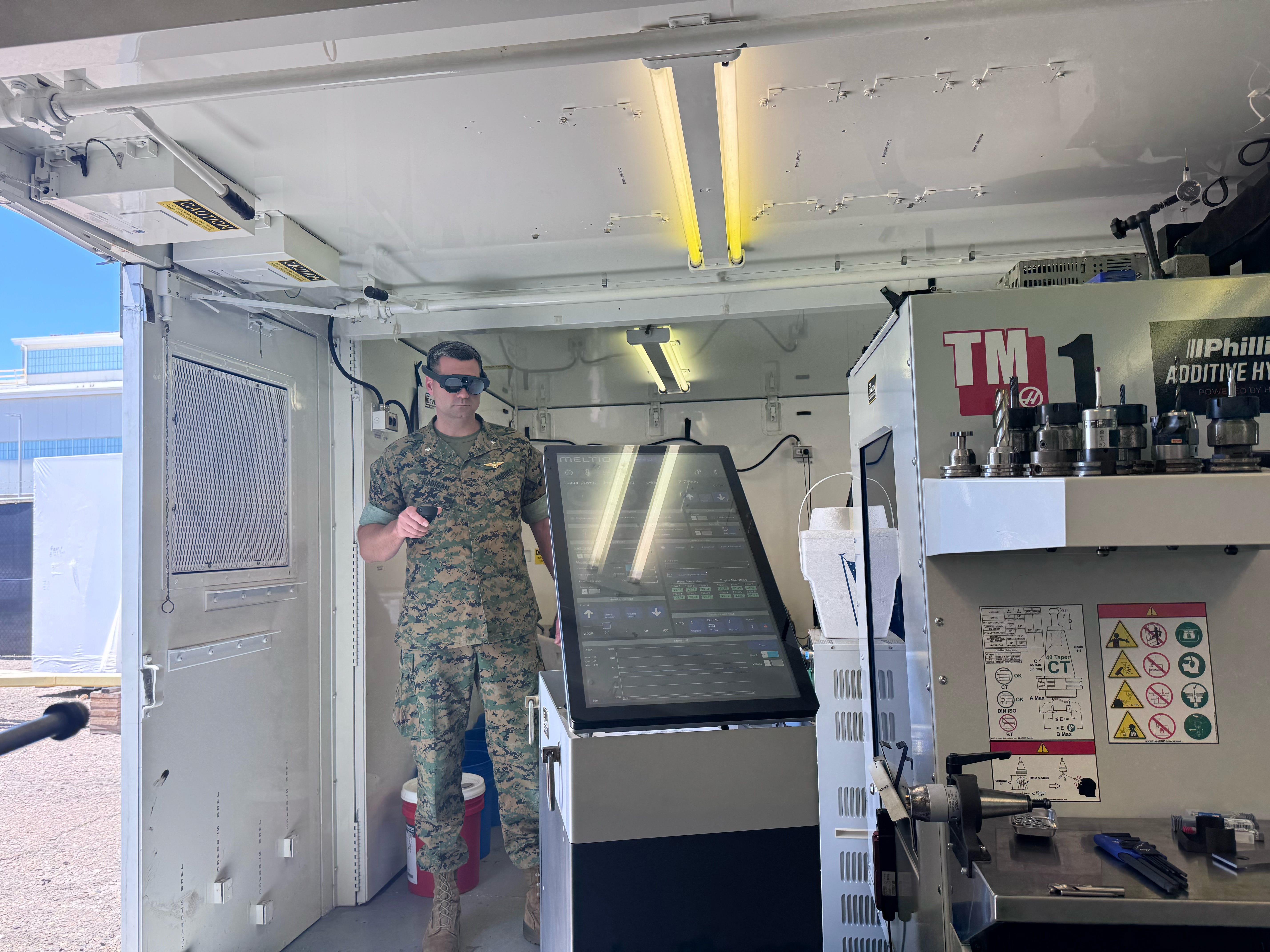 A man wearing camouflage and goggles controlling a large manufacturing machine in front of him.