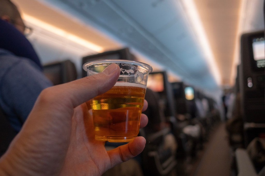 A hand holding a cup of beer on an airplane.