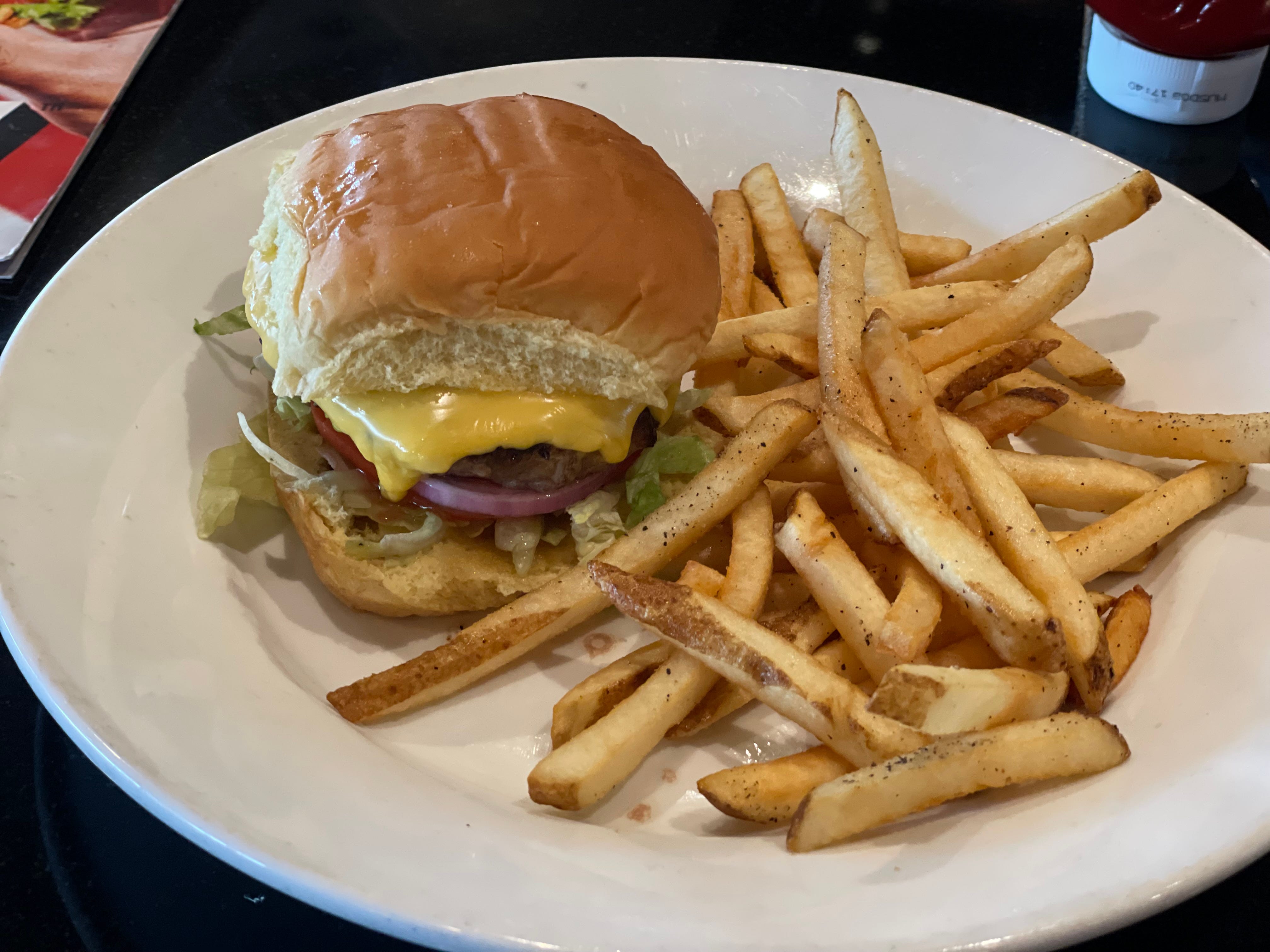 Burger with lettuce, cheese, red onion, tomato on bun with fries next to it at TGI Fridays