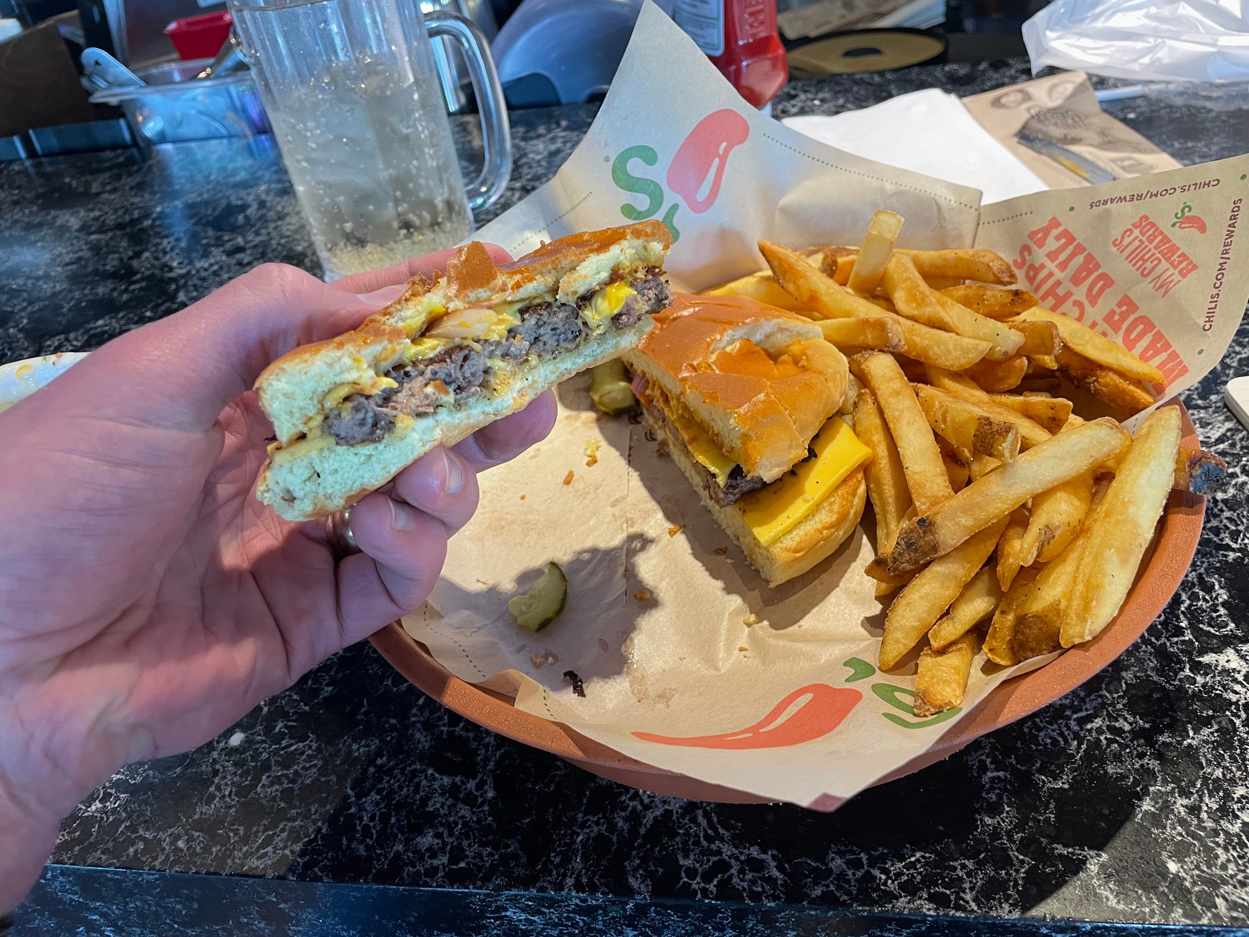 Hand holding half of burger from Chili's next to plate of fries