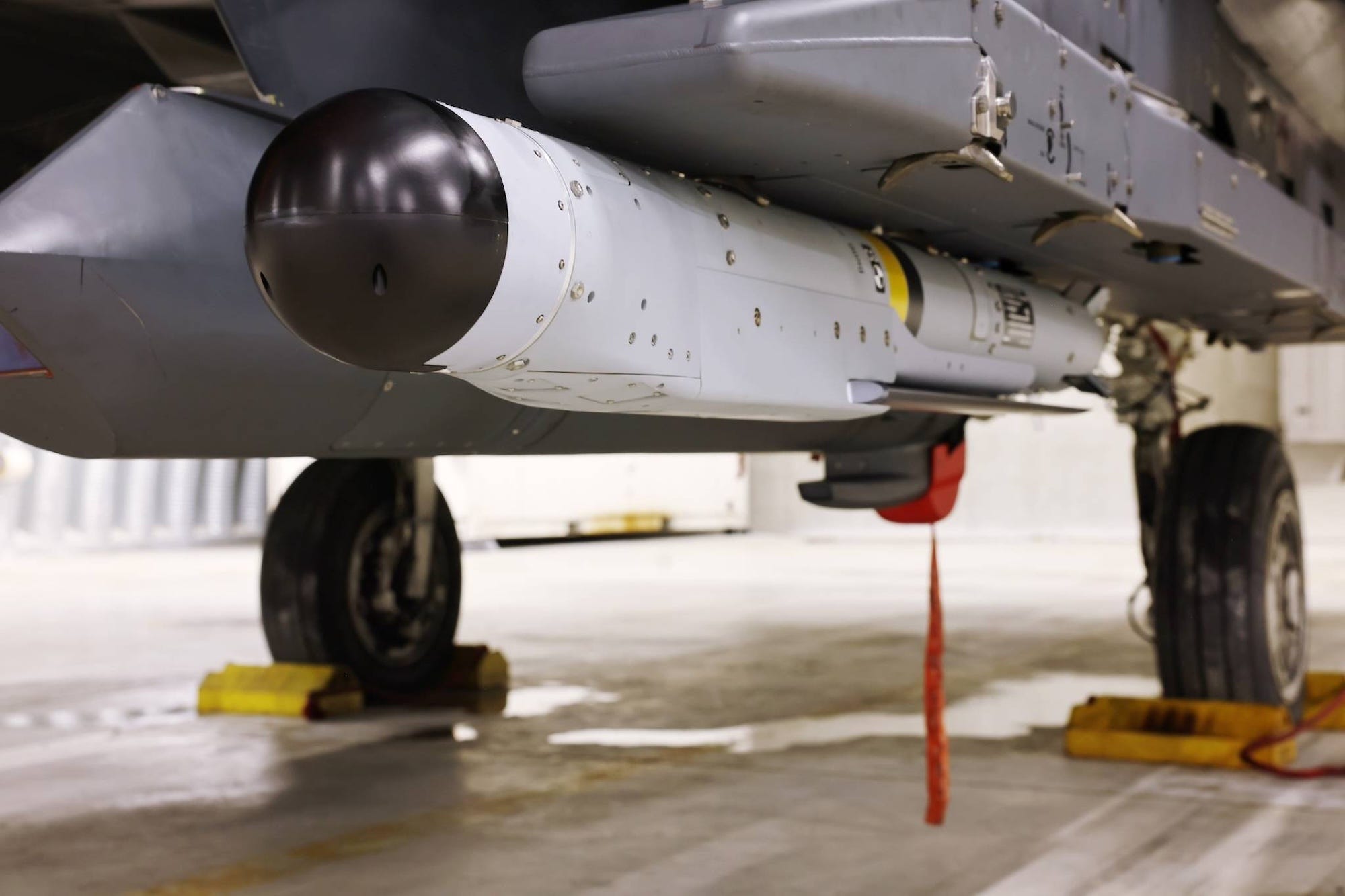 A grey bomb with a black rounded tip on the side of a grey jet on the ground