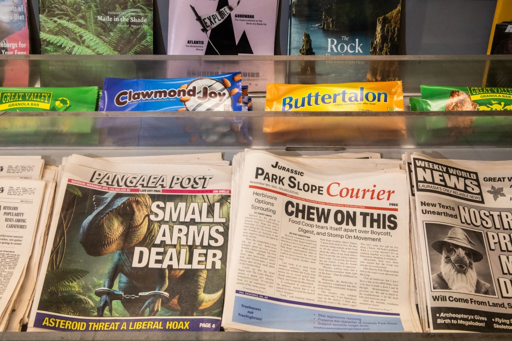 Triassic-themed newspapers and candy bars in a bodega-style display.