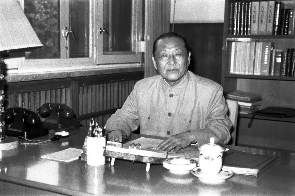 A man sits at a desk with dishes in front of him and books behind him.