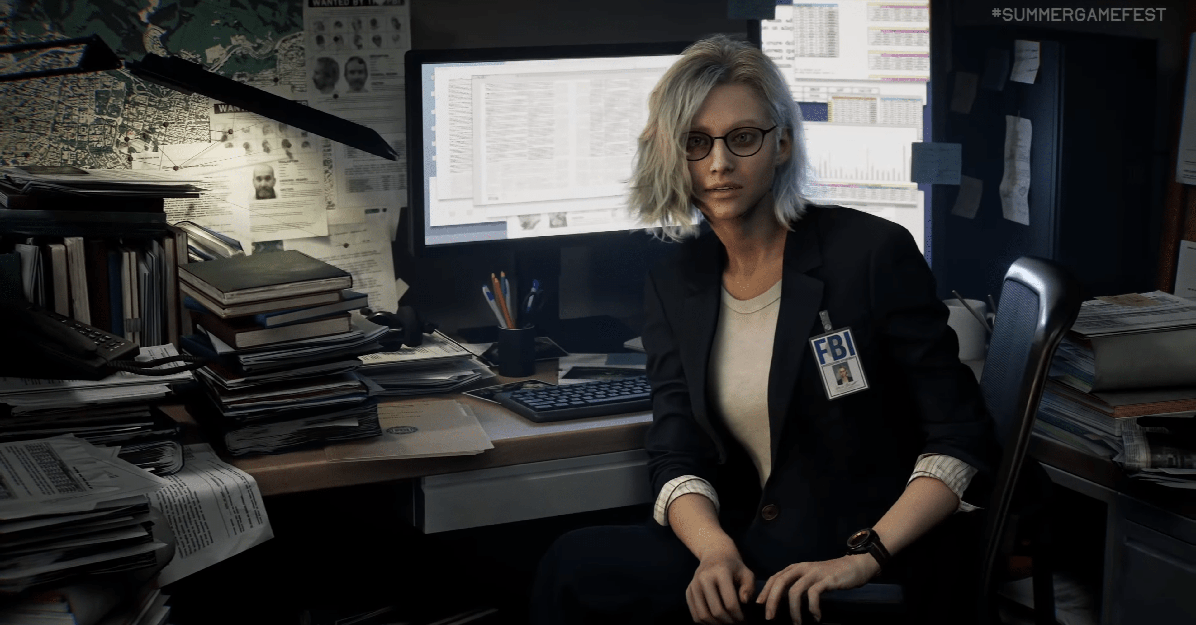 A screenshot of Grace, a blond woman with glasses, sitting in front of a messy office cubicle