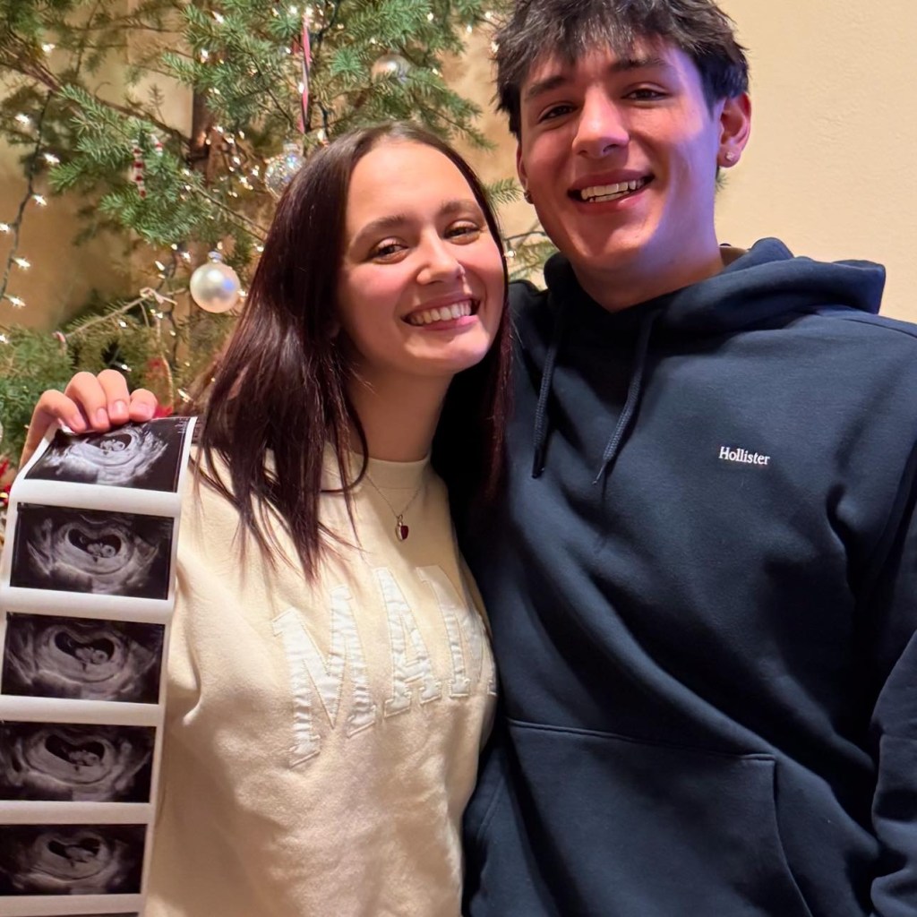 Photo of a couple holding ultrasound images in front of a Christmas tree.