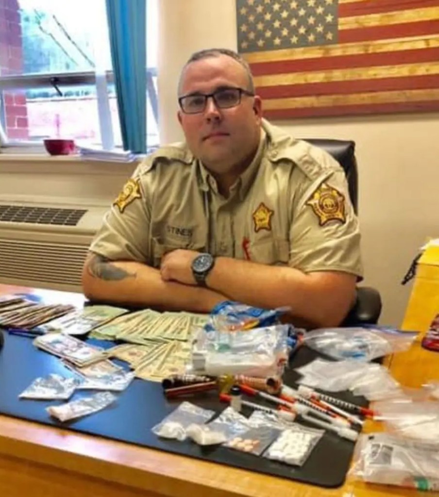 Photo of Shawn Stines, former Letcher County Sheriff, sitting at a desk with confiscated drugs and money.