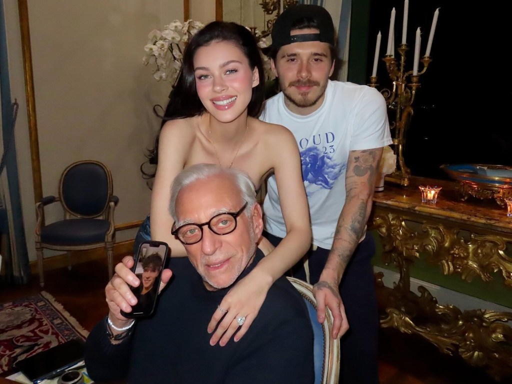 Brooklyn Beckham in a white t shirt and backwards black baseball cap Nicola Peltz in a strapless top, Nelson Peltz in a black sweater.