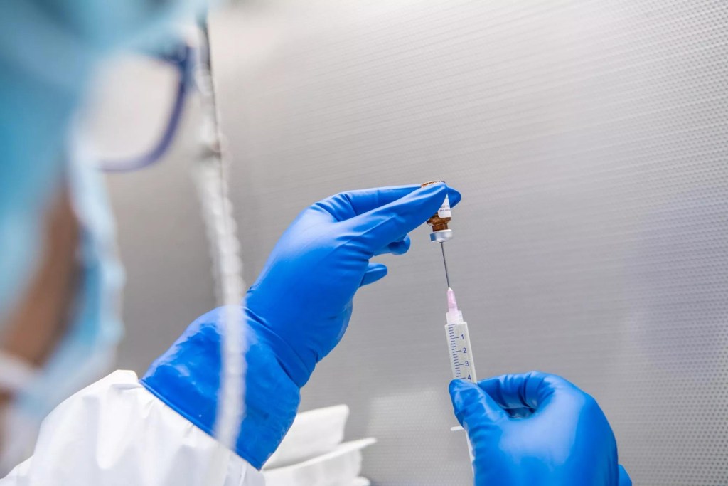 A gloved hand preparing a breast cancer vaccine.