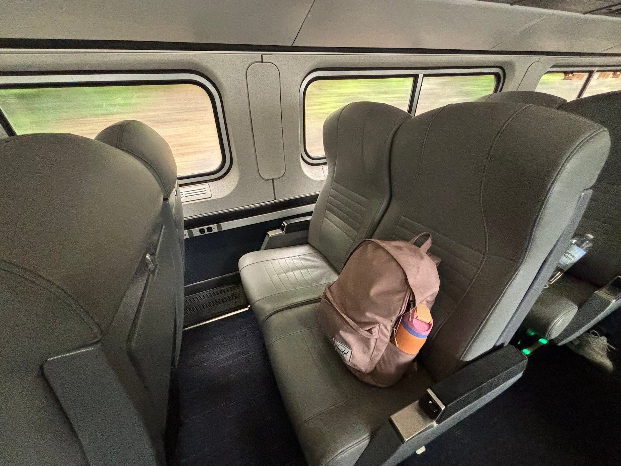 A photo of two seats on an Amtrak train. A pink backpack and water bottle sit on one seat.