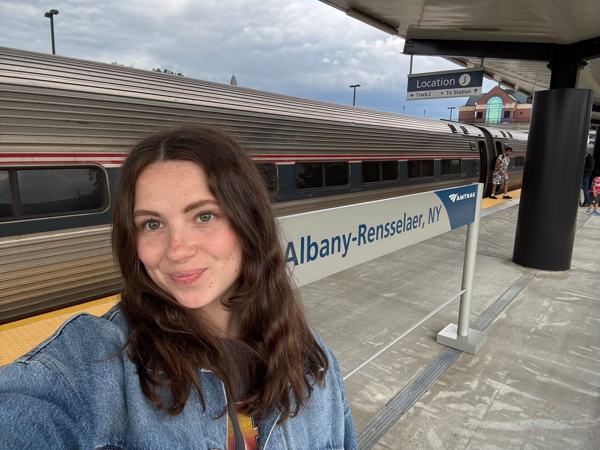A seflie of a woman in front of an Amtrak sign that says "Albany-Rensselaer, NY."