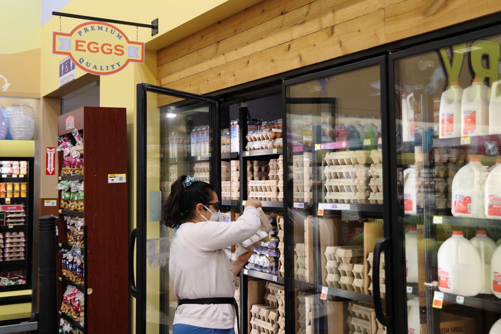 A shopper selecting eggs from a refrigerated display case in a supermarket.